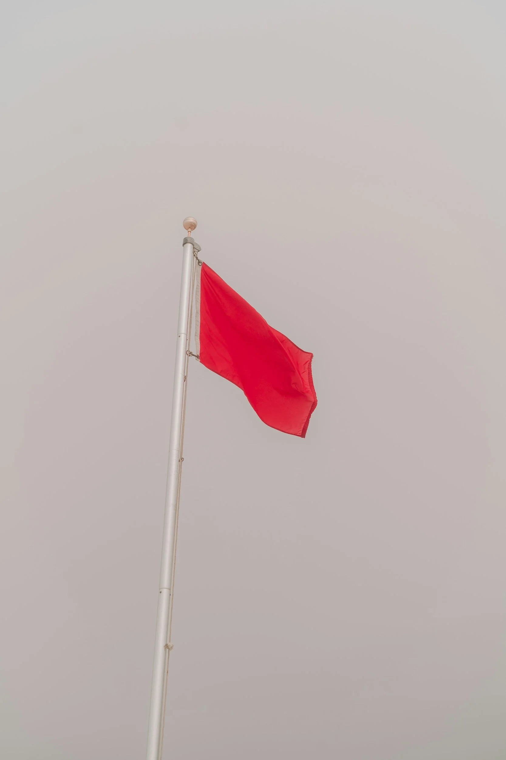 A red flag on a white pole flying against a cloudy sky.