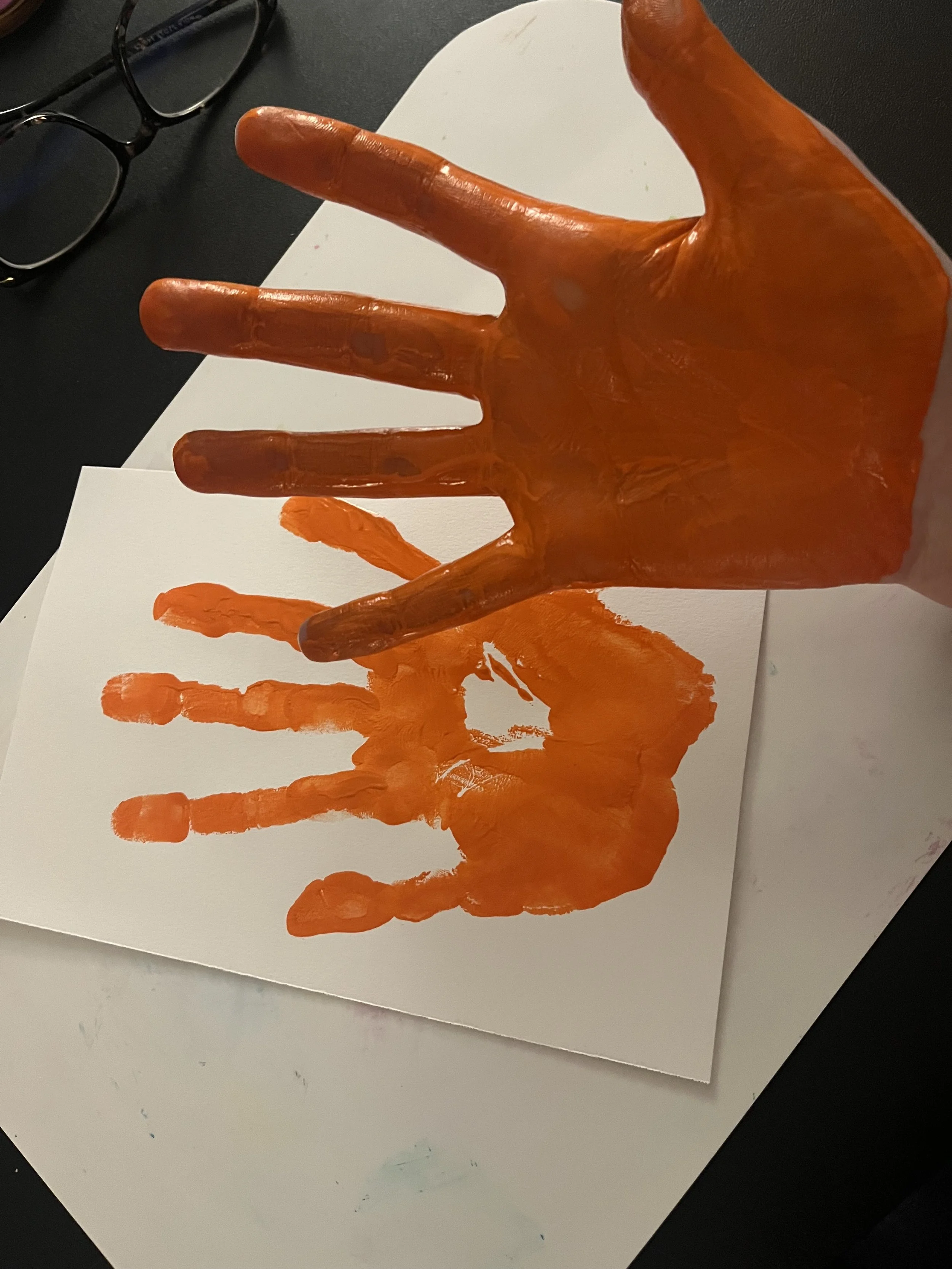 The palm of a hand painted orange above a piece of paper with an orange handprint.