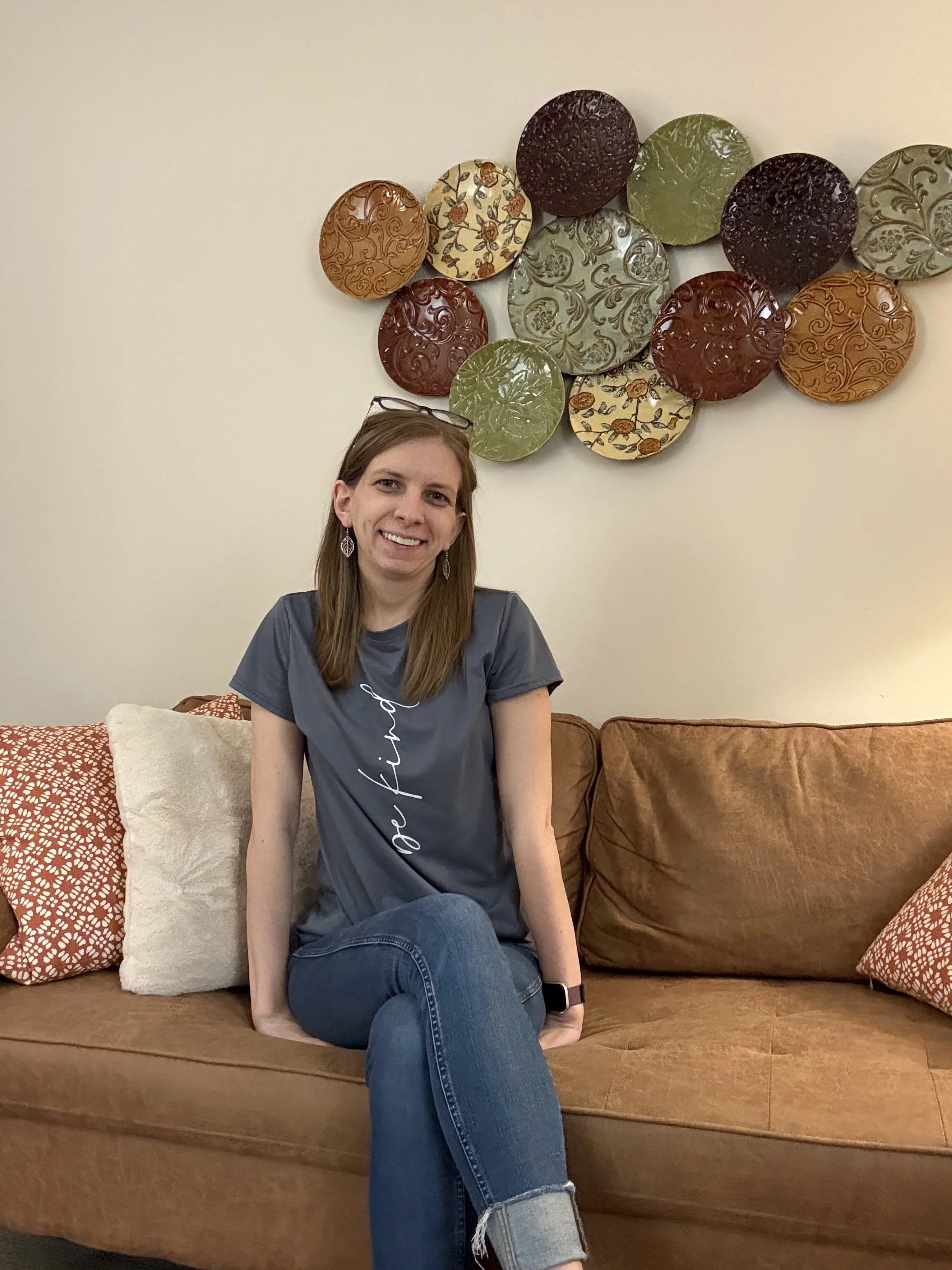 Therapist Kelly sitting on a sofa with pillows smiling.
