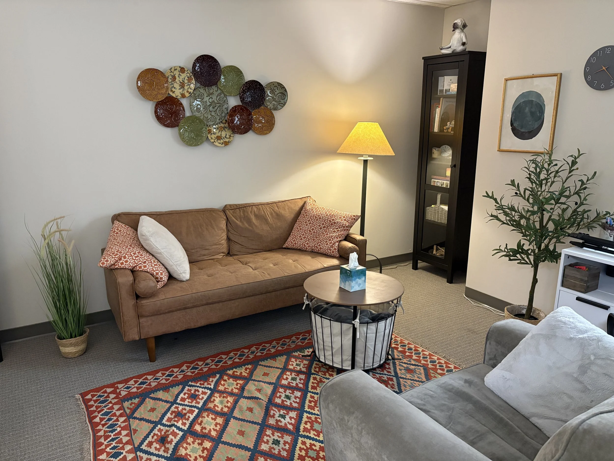 Photo of therapy space including a sofa, lamp, table with tissues, and a plant.