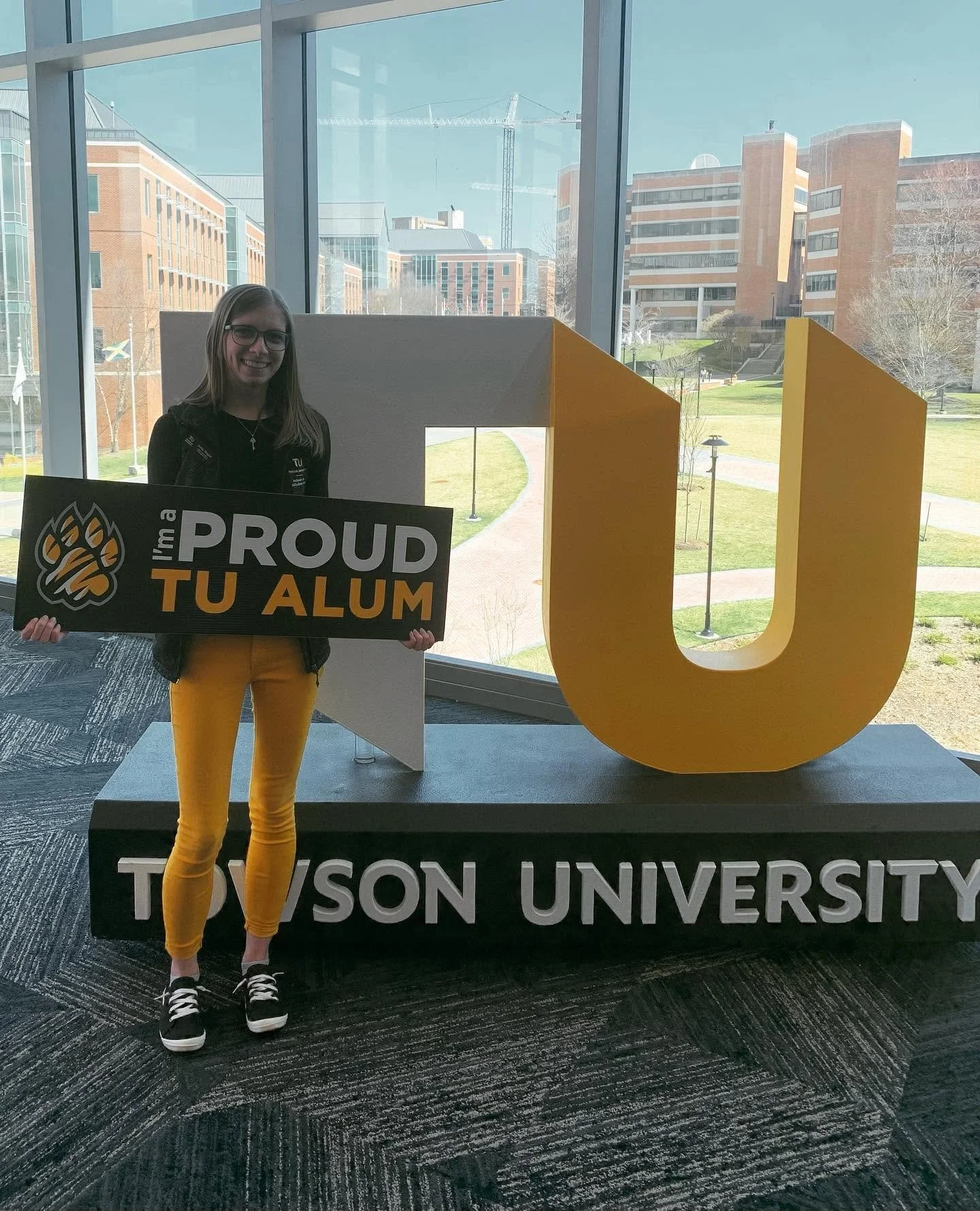 Kelly standing in front of a giant TU with a sign that says "I'm a proud TU alum"