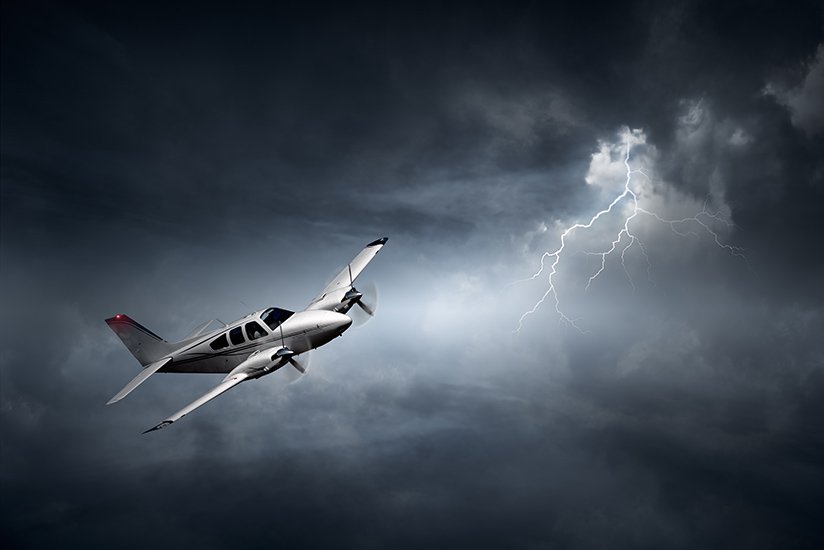 A small private airplane flying through dark stormy skies with lightning in the background.