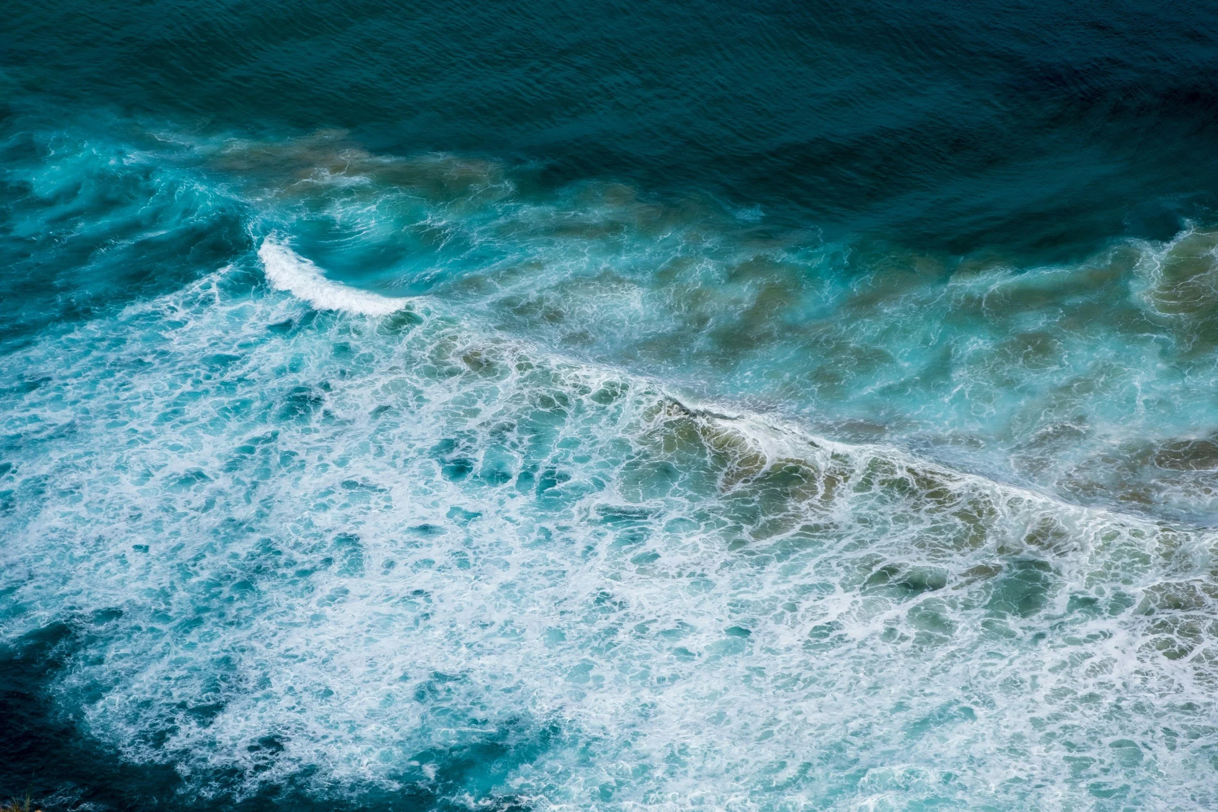 Aerial view of ocean waves with white foam and deep blue water.