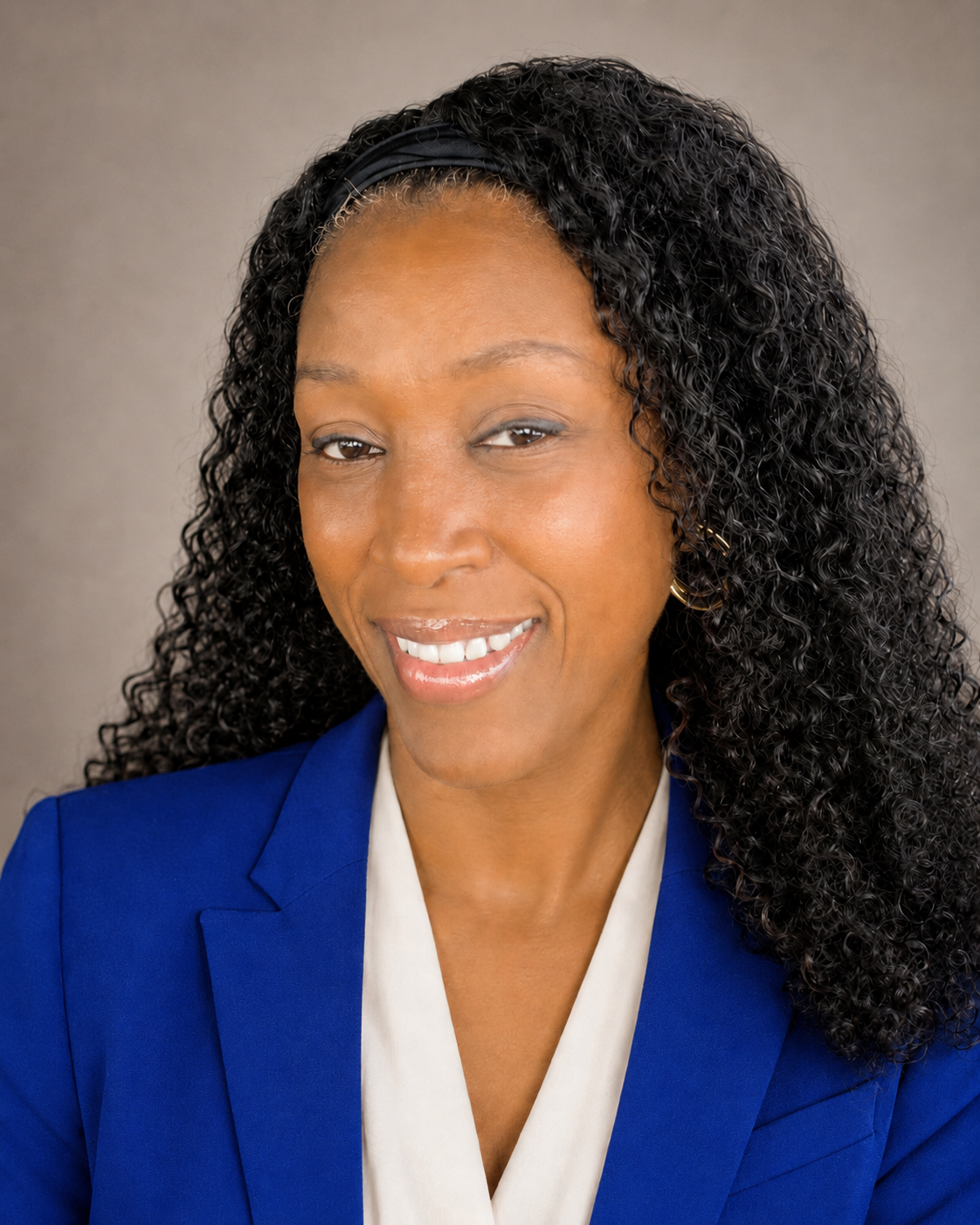 Professional woman with curly black hair, wearing a blue blazer and a white blouse, smiling.