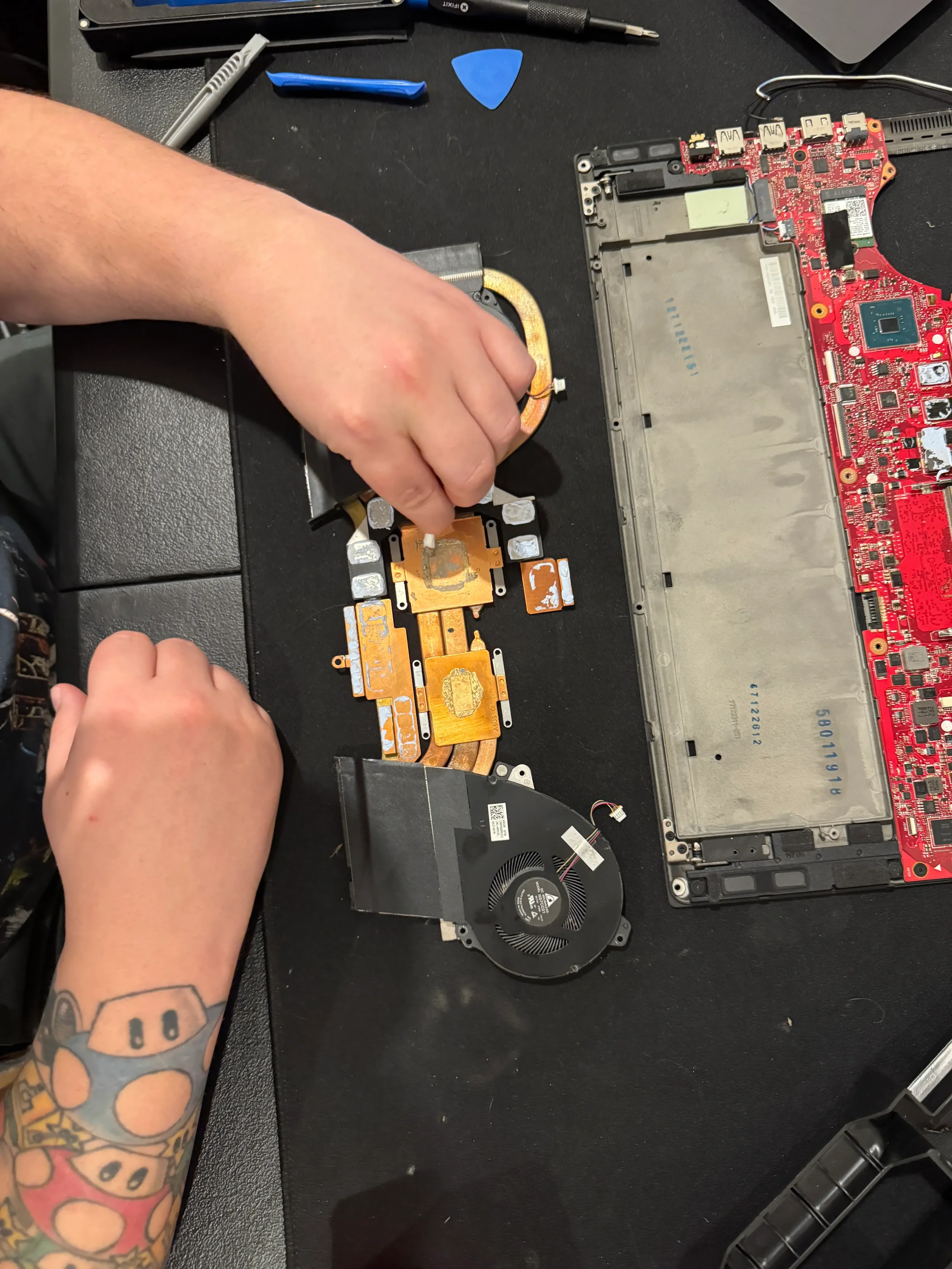 Person working on disassembling a laptop, with tools and laptop components on a black work surface.