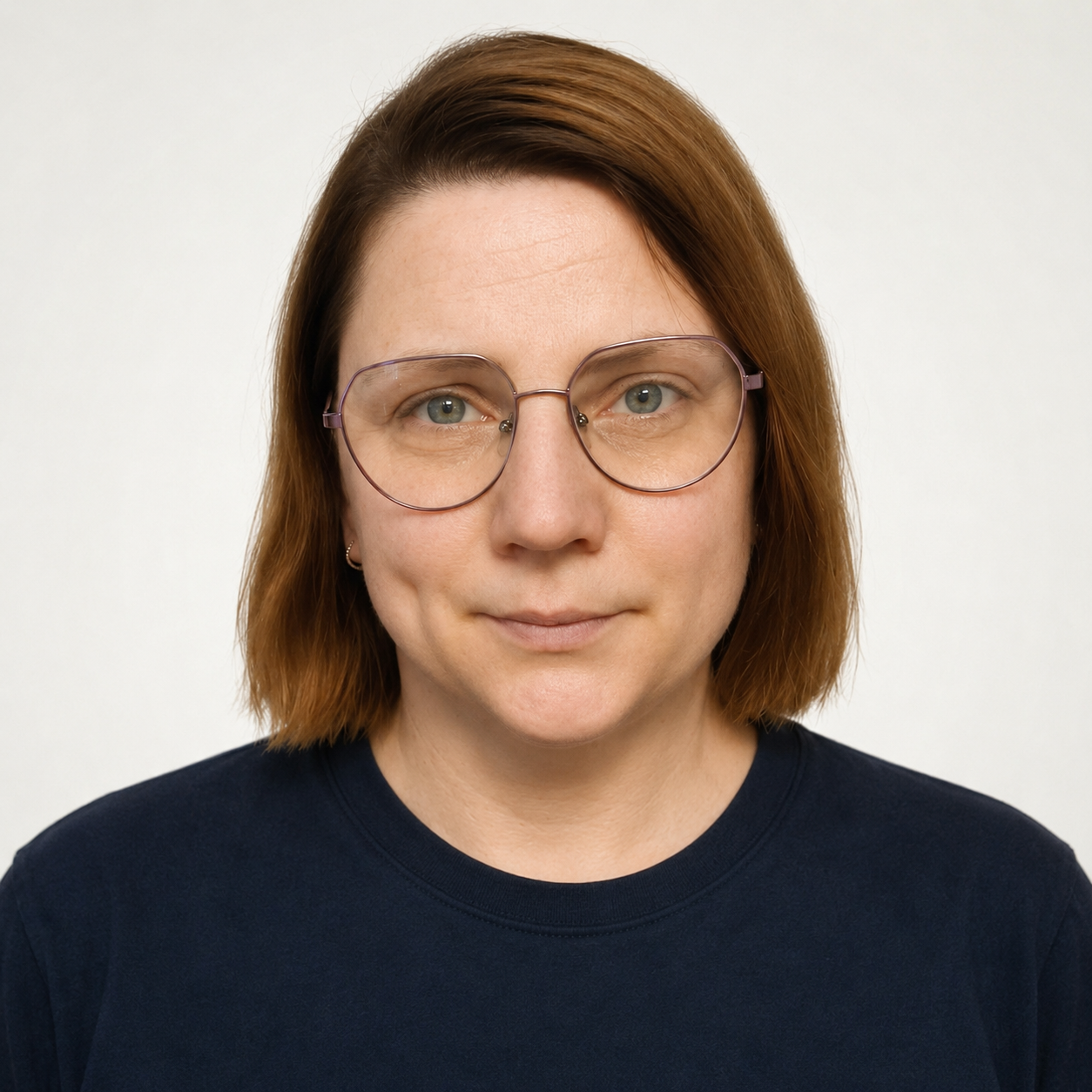 Porträt einer Frau mit kurzen, braunen Haaren, trägt große, runde Brillen, trägt ein dunkelblaues T-Shirt, vor Weißem Hintergrund.