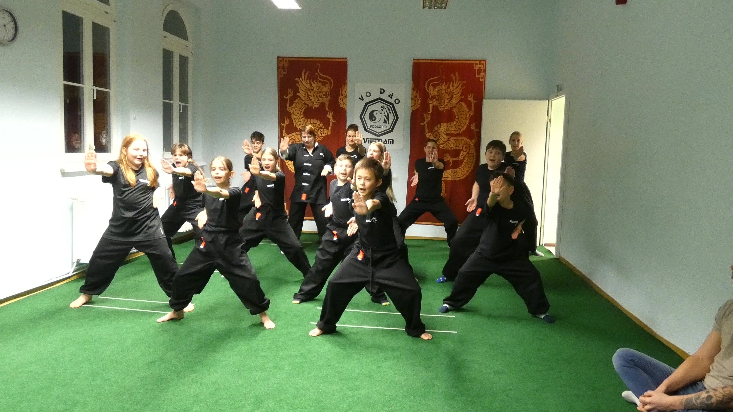 Jugendliche praktizieren Taekwondo in einem Trainingsraum mit asiatischen Dekorationen.