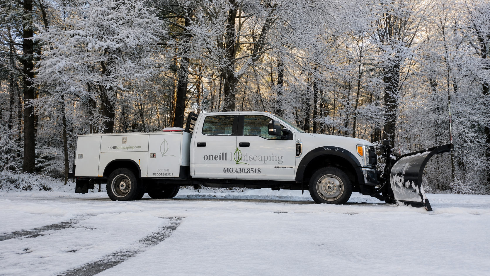 O'Neill Landscaping snow plow truck with the logo and contact information for oneilllandscaping is parked on snow-covered ground in front of a forest of snow-covered trees during winter.