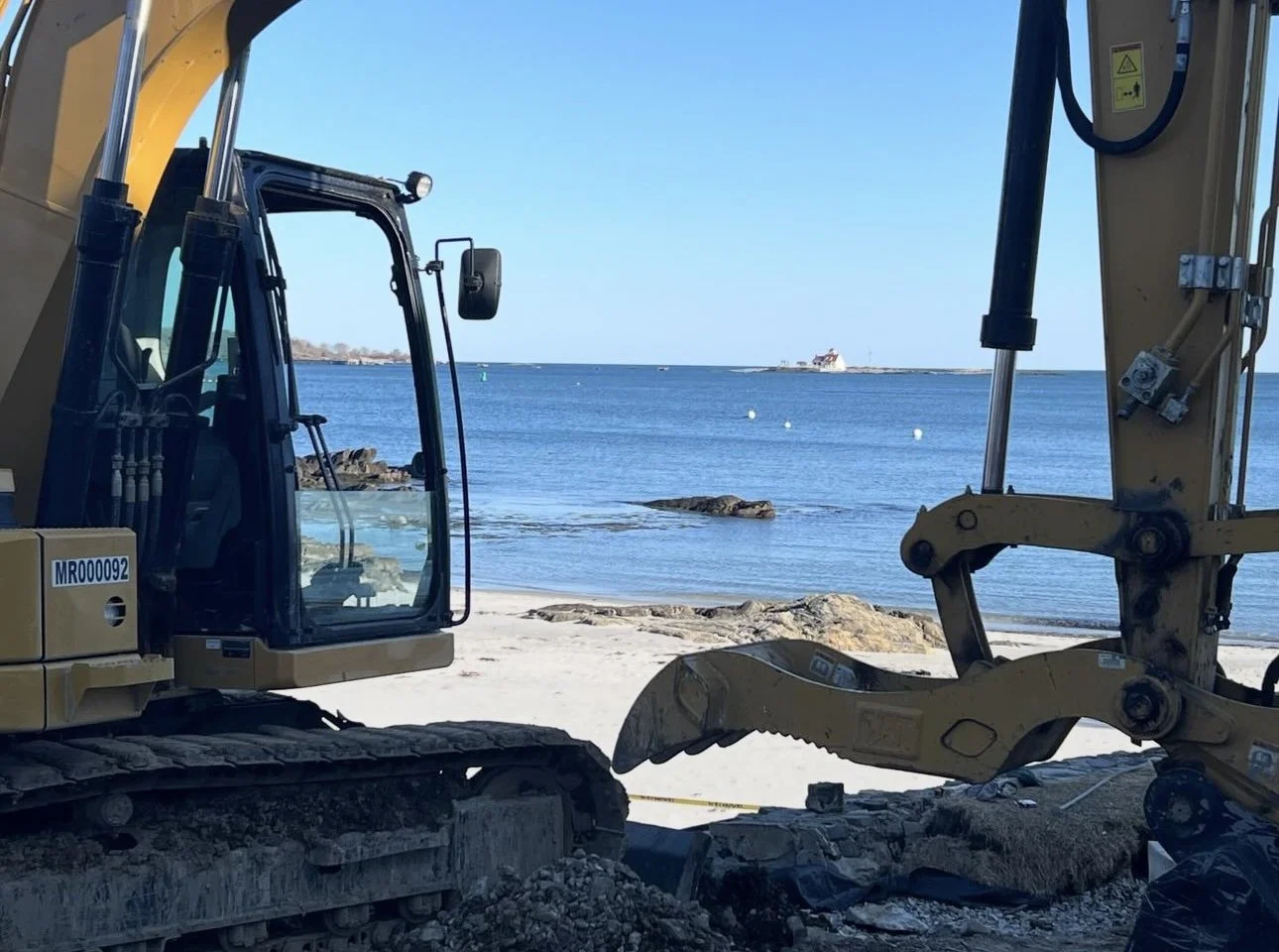 Construction equipment with a view of the ocean and a building on an island in the background.