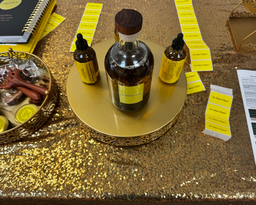 A tabletop display with three small bottles of a liquid, likely medicine or oil, on a gold-colored round tray. There are yellow labels on strips of paper and a foliated object in a decorative bowl on the left. The table has a glittery gold and brown surface.