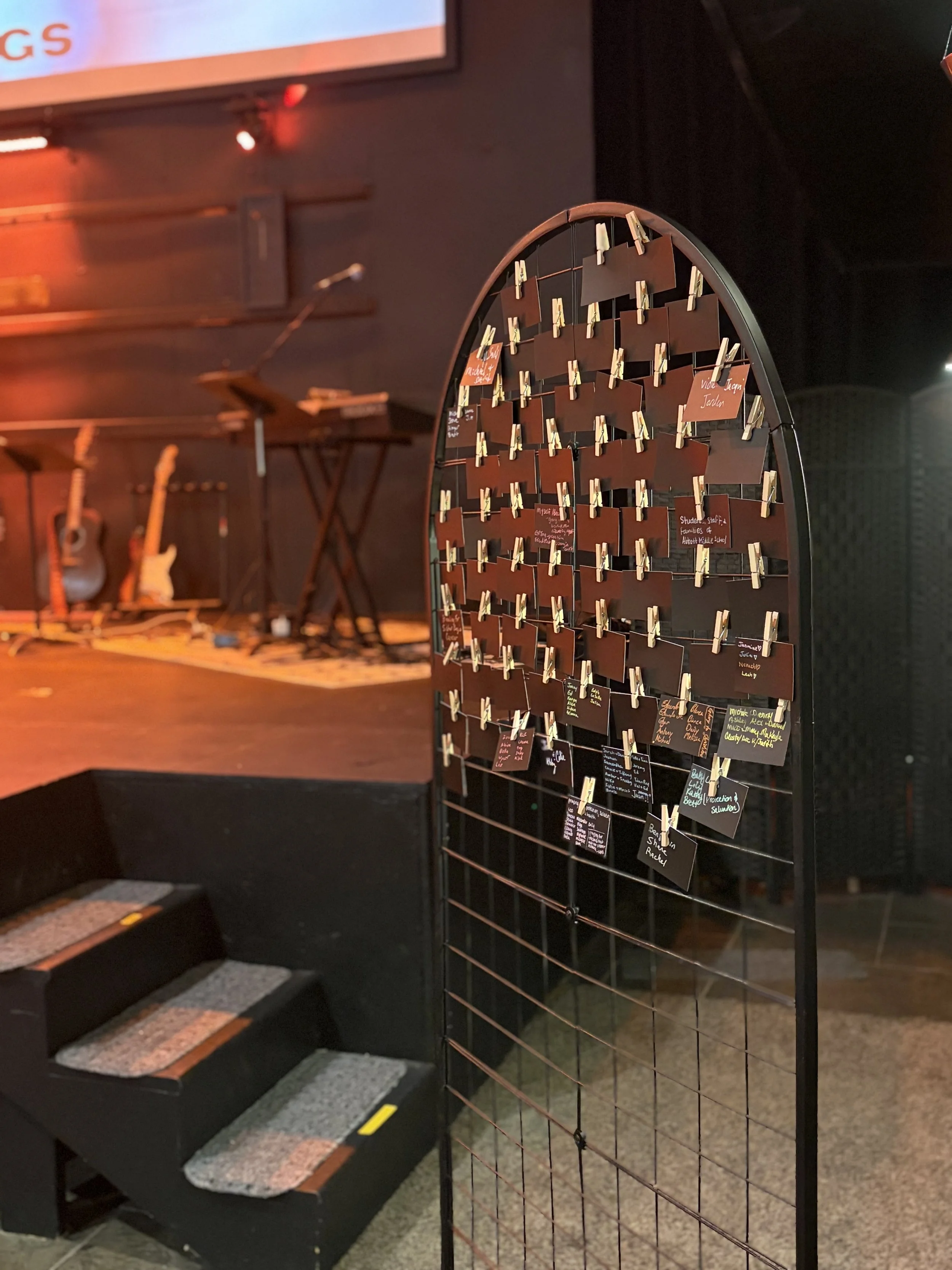 A music venue stage with musical instruments and a wire grid with small colorful notes or cards attached with clothespins in front of the stage.