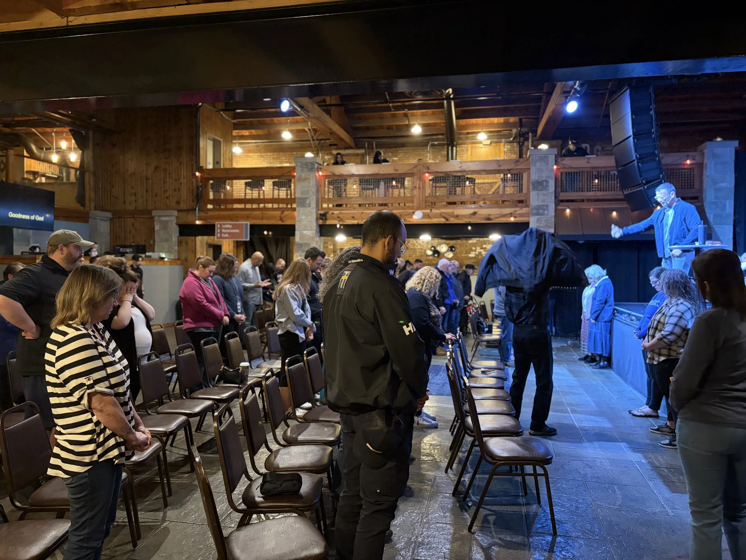 People praying in a church during a service with a speaker and a large audience.
