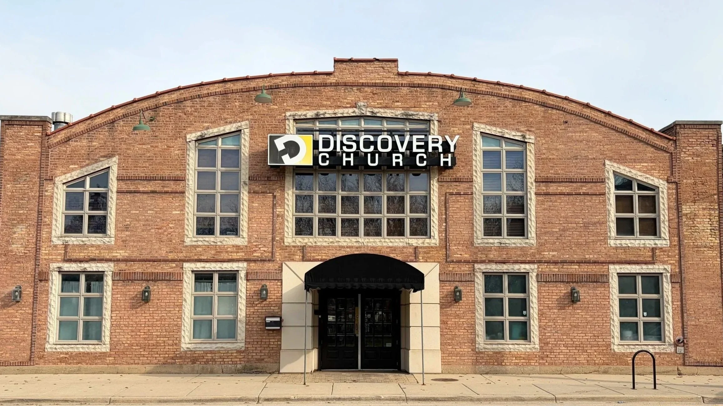 The facade of Discovery Church building made of red brick with multiple windows and a sign reading "Discovery Church" above the entrance.
