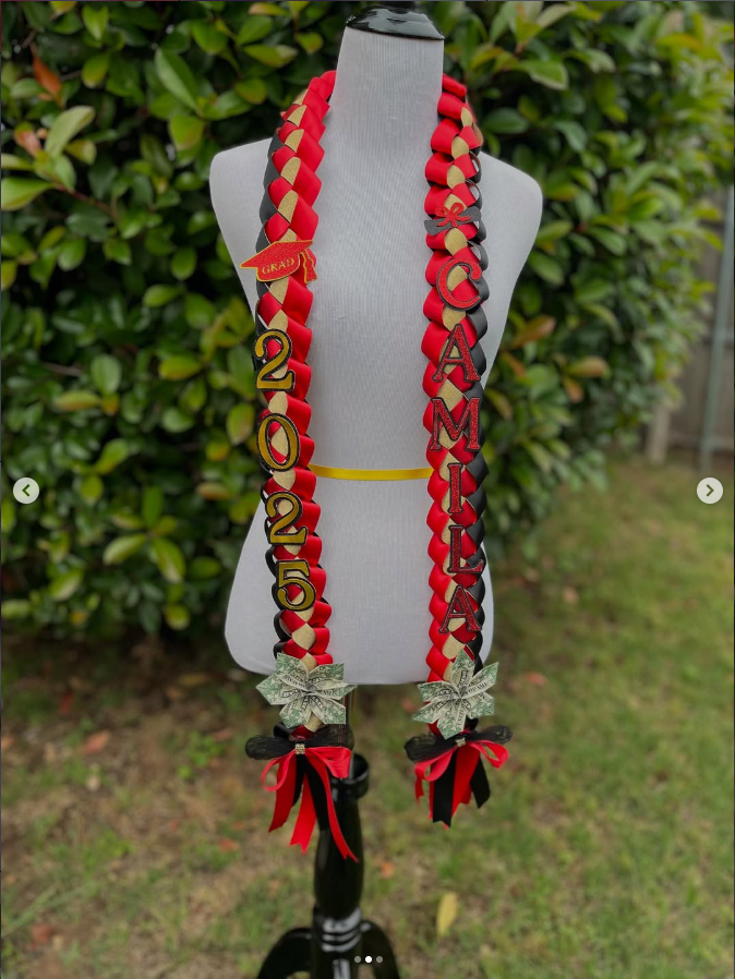 Graduation lei and decorations with the words 'Class of 2025', 'Grad', and 'Amila' on a mannequin outside with greenery in the background.
