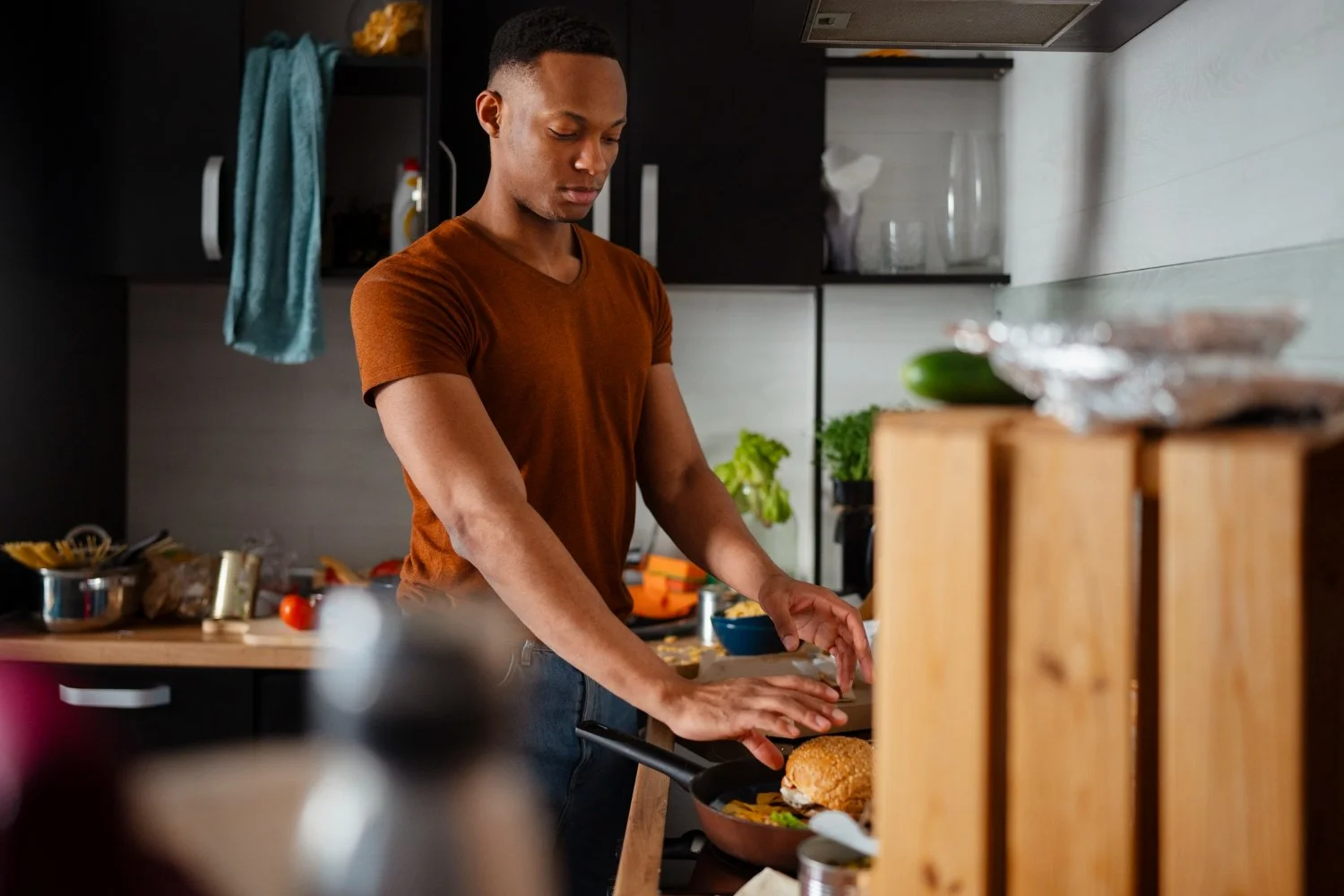 A young man cooking in a modern kitchen, frying a sandwich on a skillet with vegetables inside.