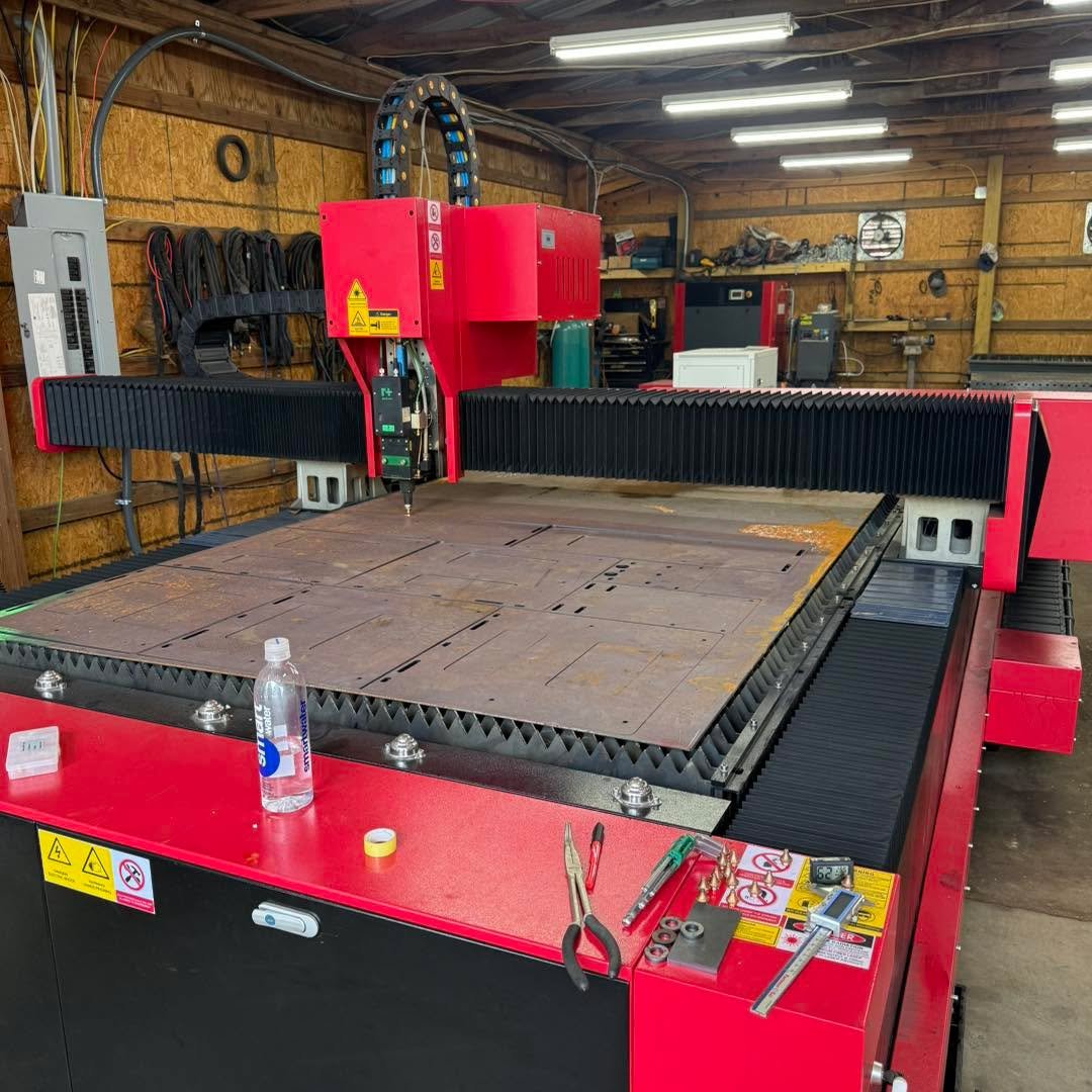 Large red CNC laser cutting machine in a workshop with tools and electrical equipment.