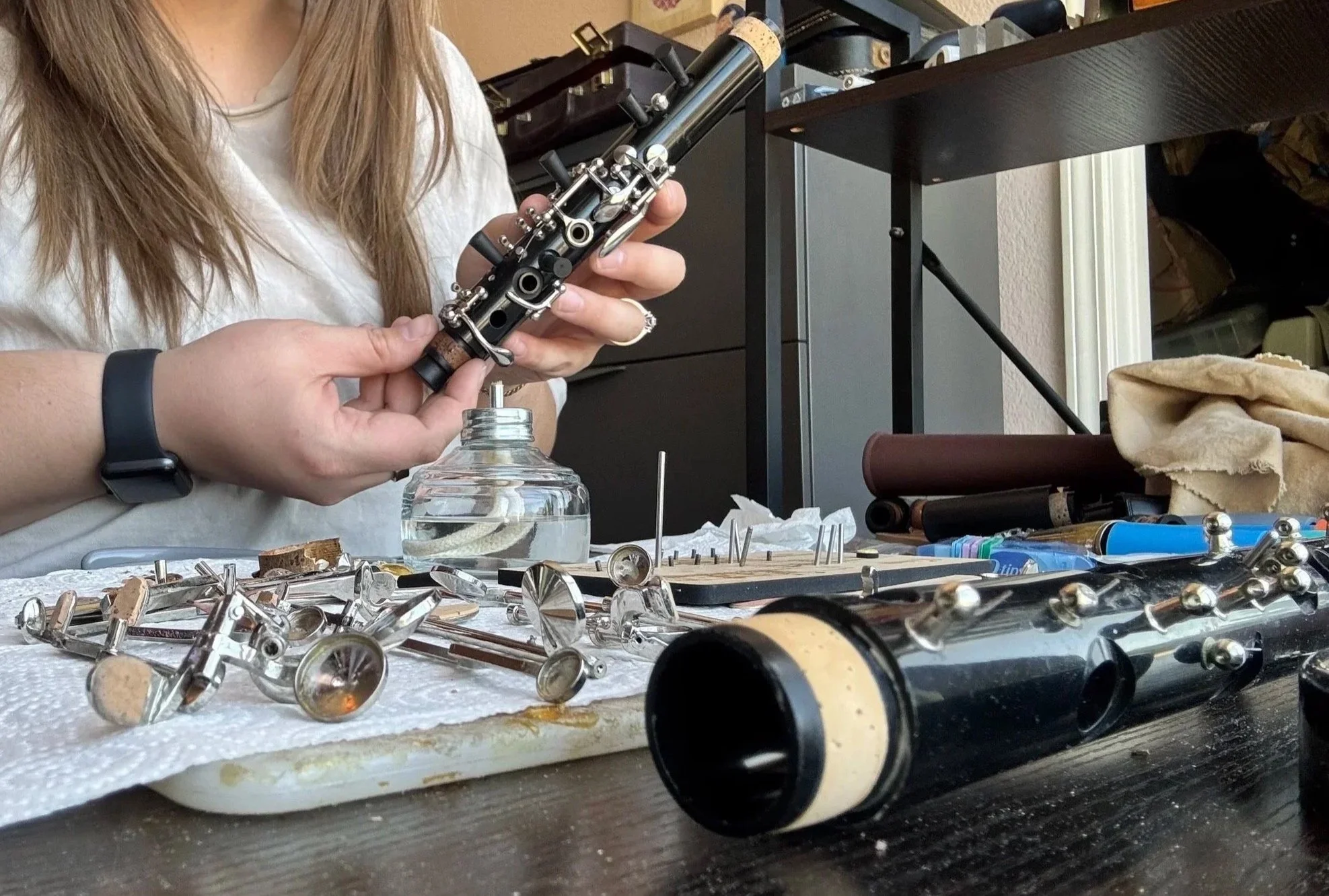 Person working on a disassembled telescope at a workbench with various telescope parts and tools scattered around.
