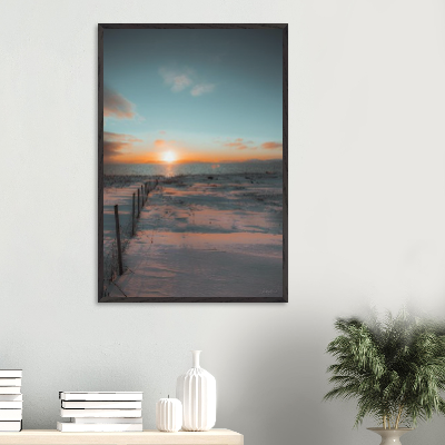 Sunset over a snowy landscape with a fence in the foreground.