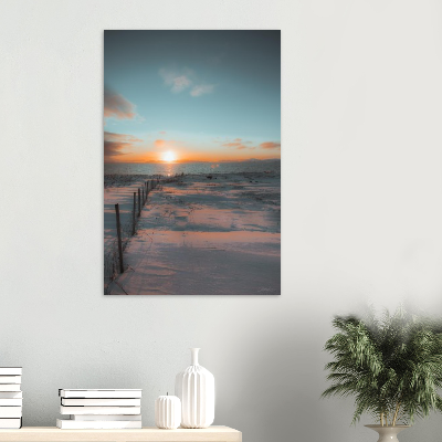 Sunset over a snowy beach with wooden posts and a cloudy sky.