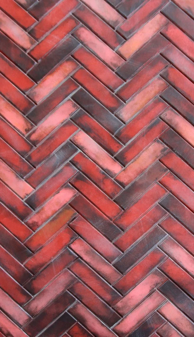 Close-up view of a herringbone pattern brick wall with red and dark gray bricks.