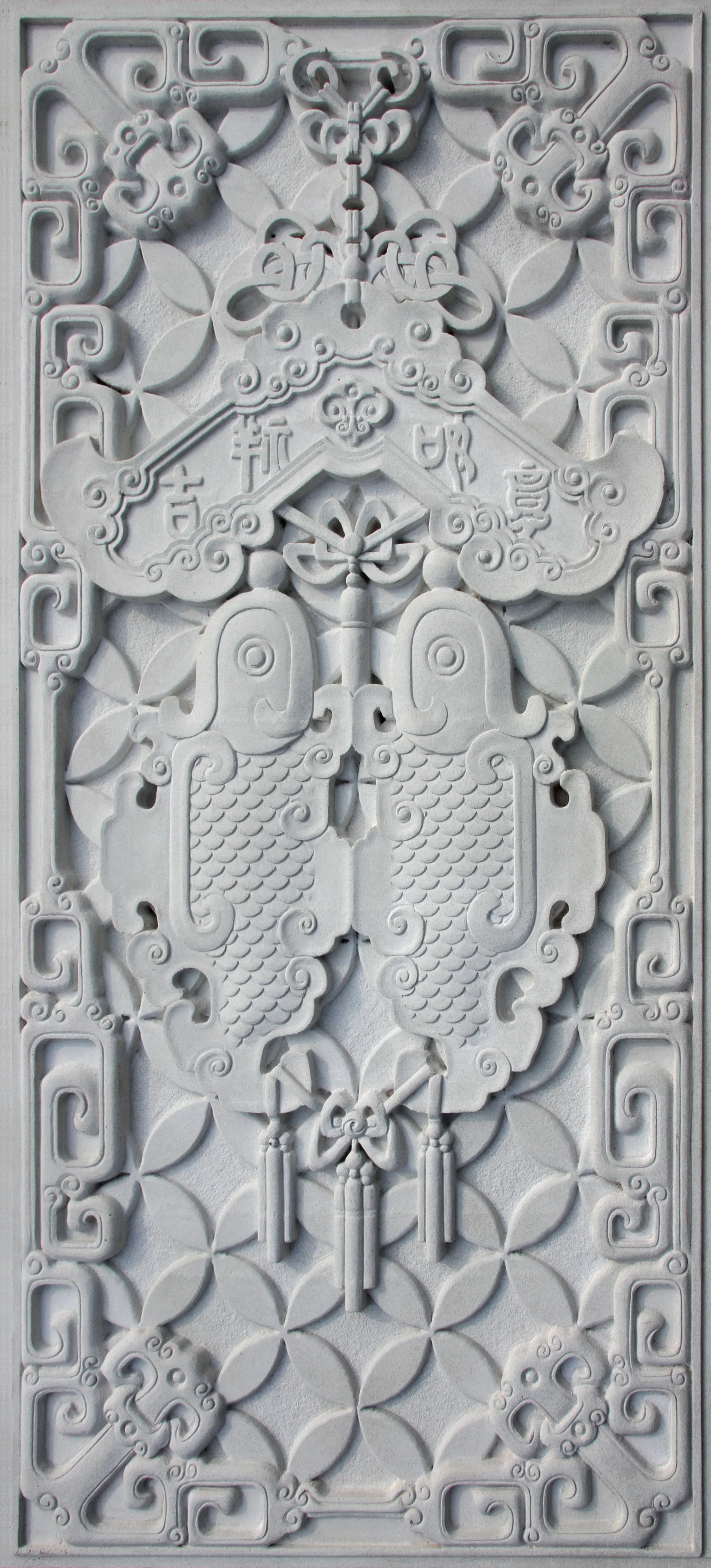 Intricate white carved panel featuring stylized fish, clouds, and Chinese characters arranged symmetrically with floral and geometric patterns.