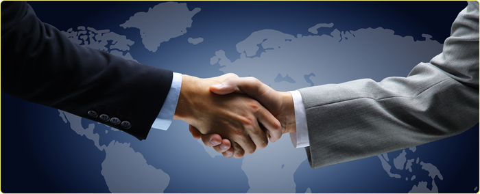 Two people in business suits shaking hands with a world map in the background.