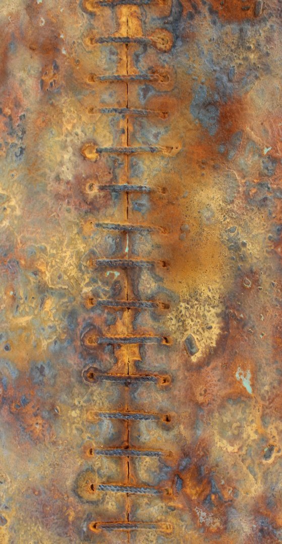 Close-up of rusty, weathered metal surface with a vertical series of evenly spaced, elongated holes connected by small, horizontal bars.