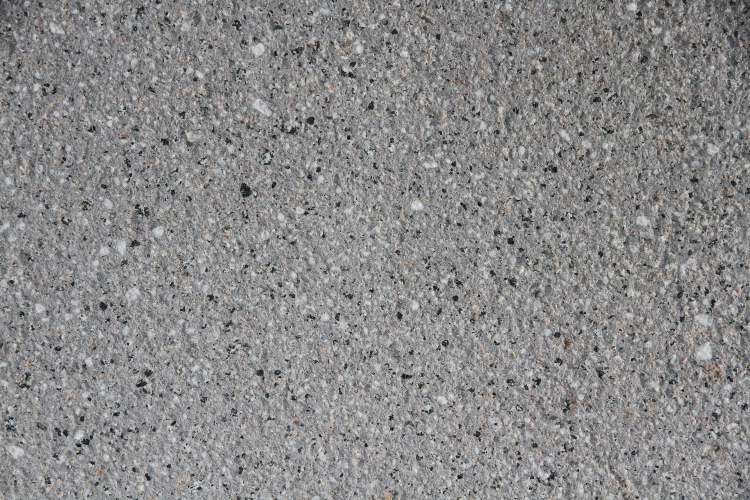 Close-up view of gray concrete pavement with small embedded stones and gravel.