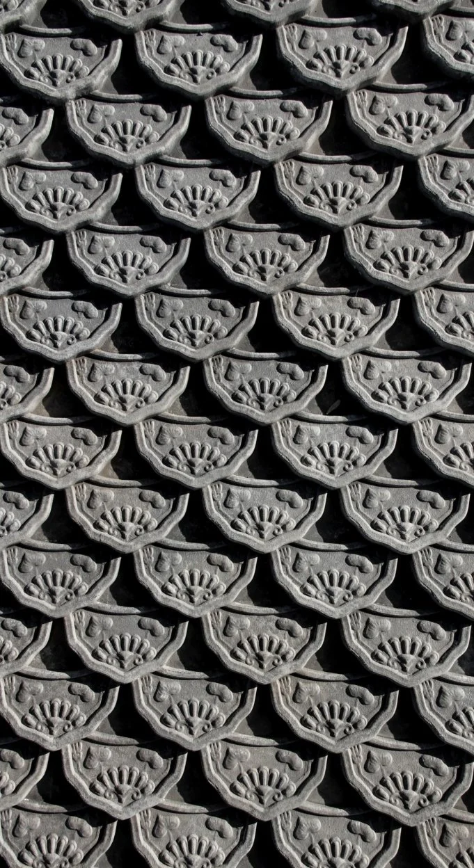 Close-up of a pattern of gray, decorative roof tiles with a scalloped fan design and symmetrical detailing.