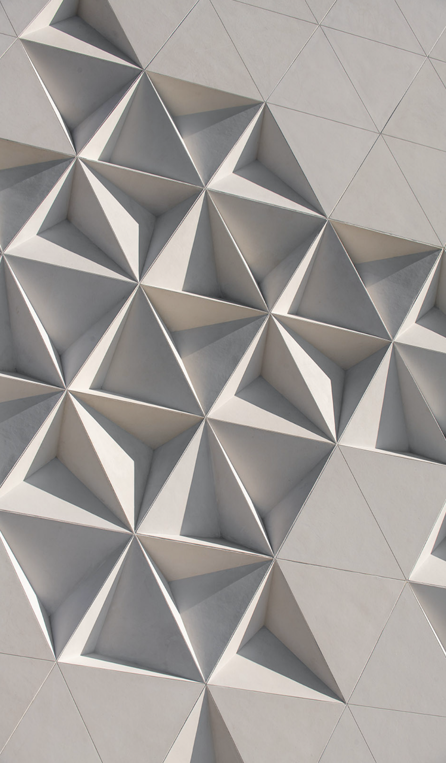 Close-up of a modern geometric architectural wall with 3D triangular and diamond-shaped patterns in shades of white and light gray.