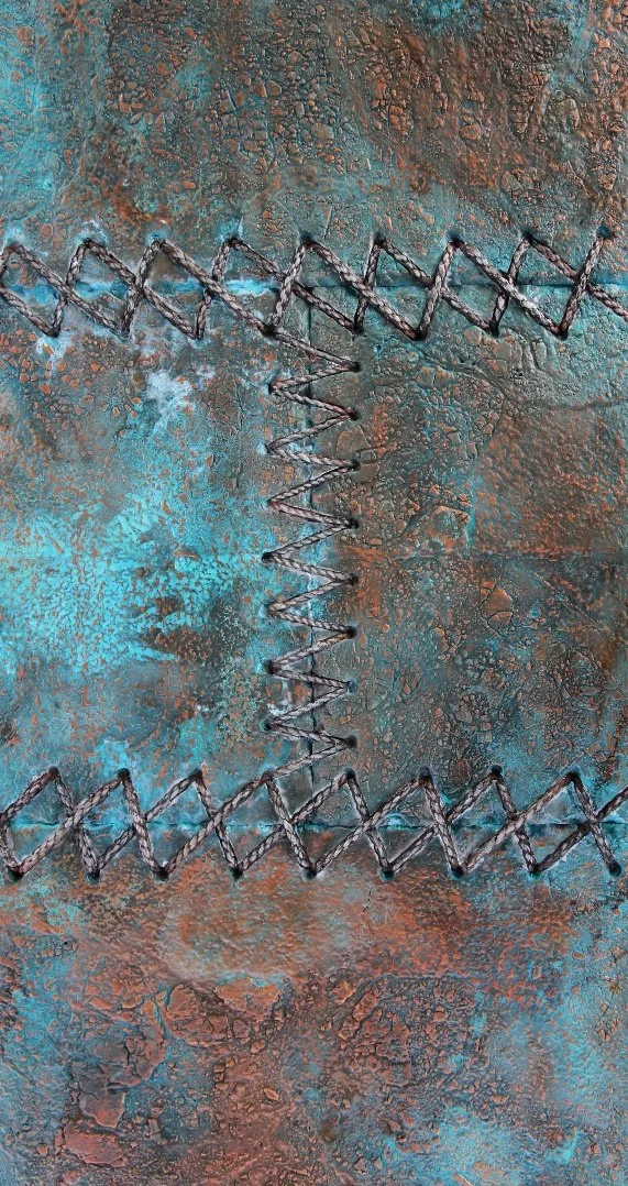 Close-up of a rusted metal surface with textured, cracked blue and brown corrosion and raised, zigzagging wire elements.