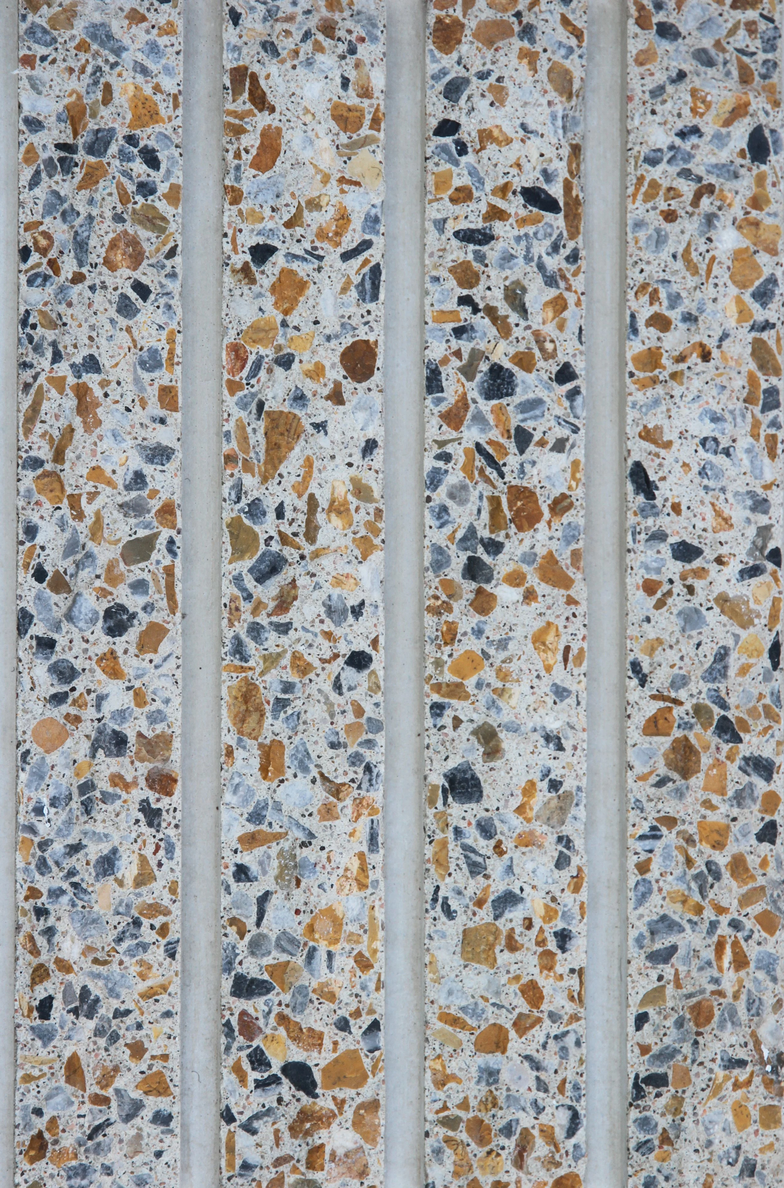 Close-up of a textured surface with colorful gravel embedded in concrete, separated by vertical concrete strips, resembling a terrazzo or speckled wall.
