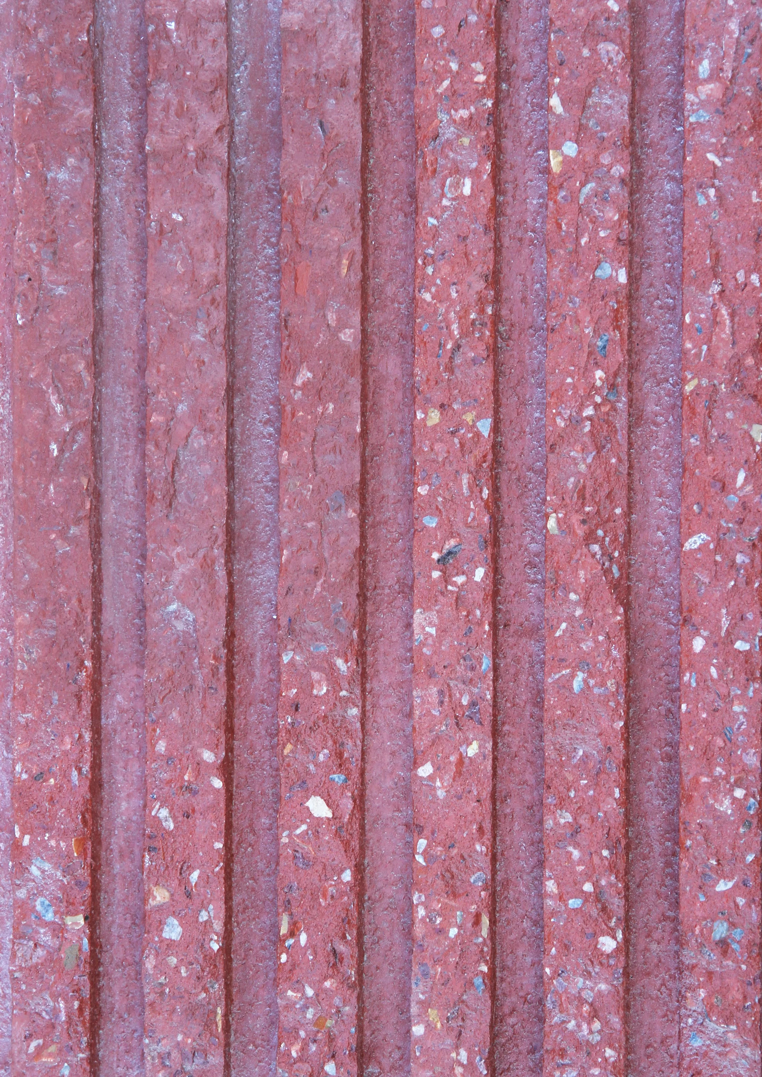 Close-up of a pink concrete sidewalk with evenly spaced rectangular slabs, embedded with small multicolored stones.