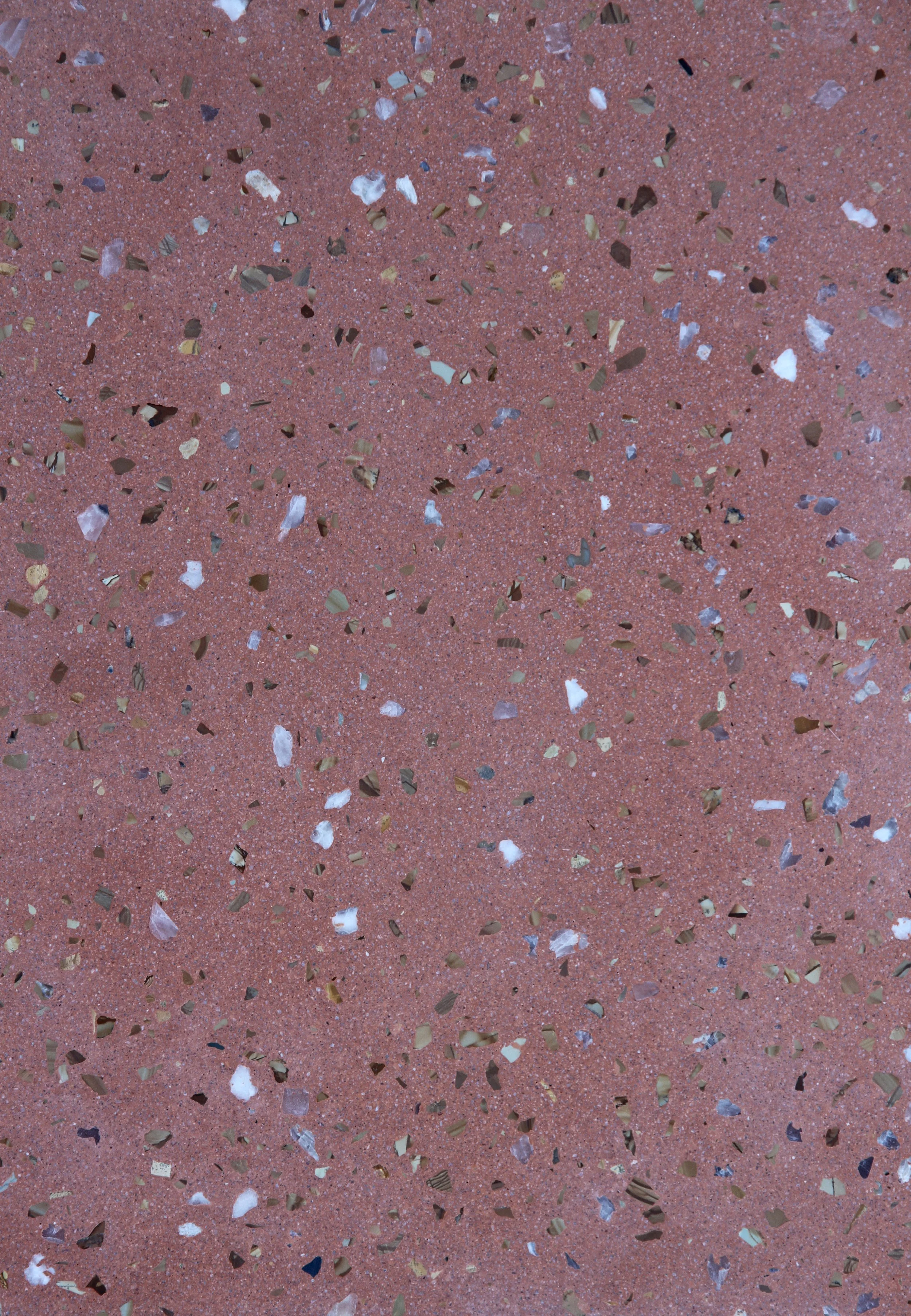Close-up of a red terrazzo flooring with multicolored fragments of marble and stone embedded in the surface.