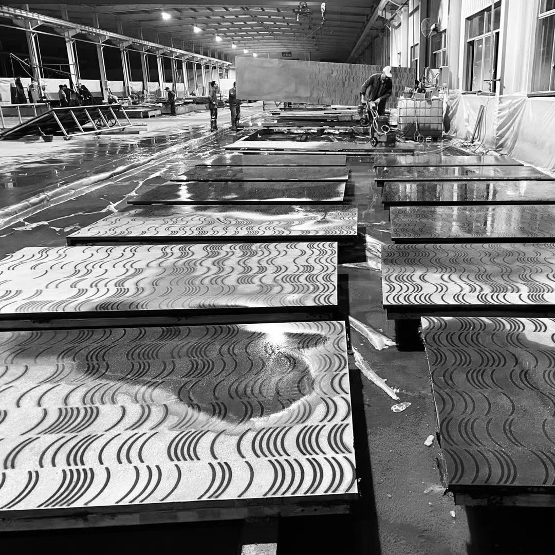 Workers in a factory or warehouse space assembling or inspecting patterned panels on tables, with large windows and industrial equipment visible.