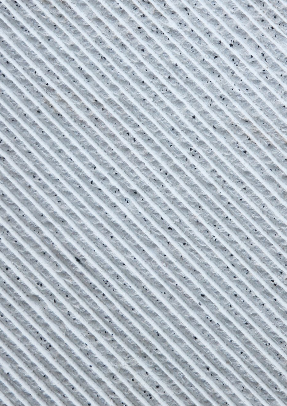 Close-up of a textured surface with diagonal ridges and small black specks.