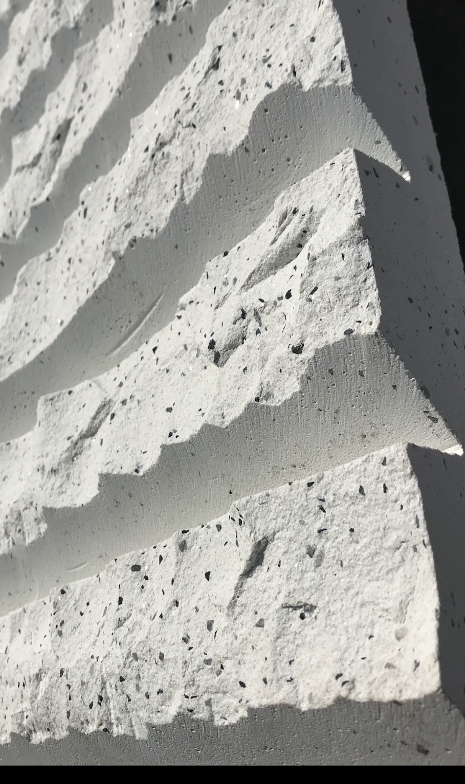 Close-up of textured white concrete wall with black speckles and shadows.