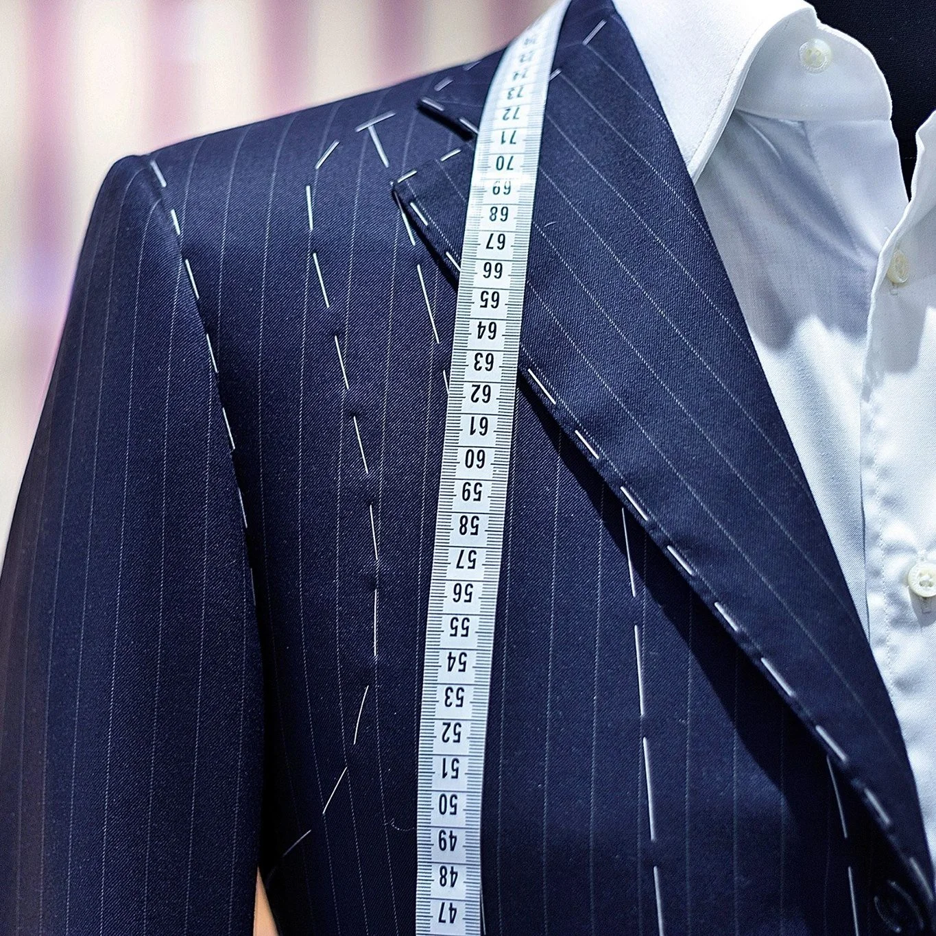 Close-up of a man wearing a navy blue pinstripe suit with a white shirt, with a measuring tape draped over his shoulder.