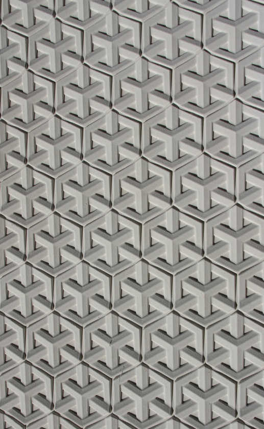 Close-up of a patterned surface with three-dimensional geometric shapes resembling interconnected Y-shapes or arrows, repeated uniformly across the surface.