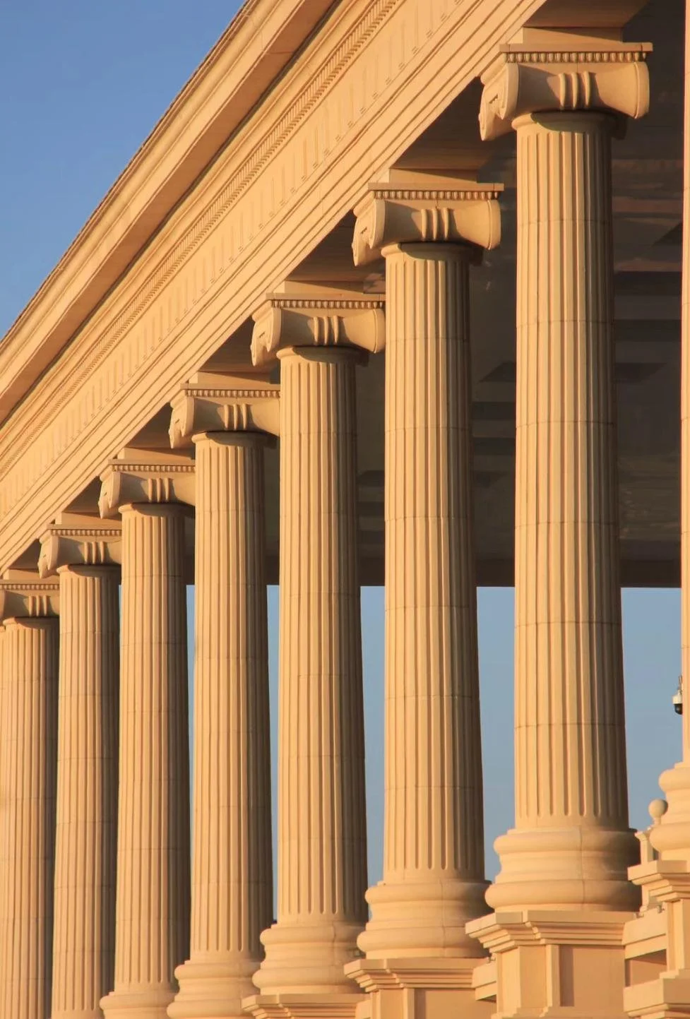 Close-up of classical Greek-style columns supporting a building, with a clear blue sky in the background.