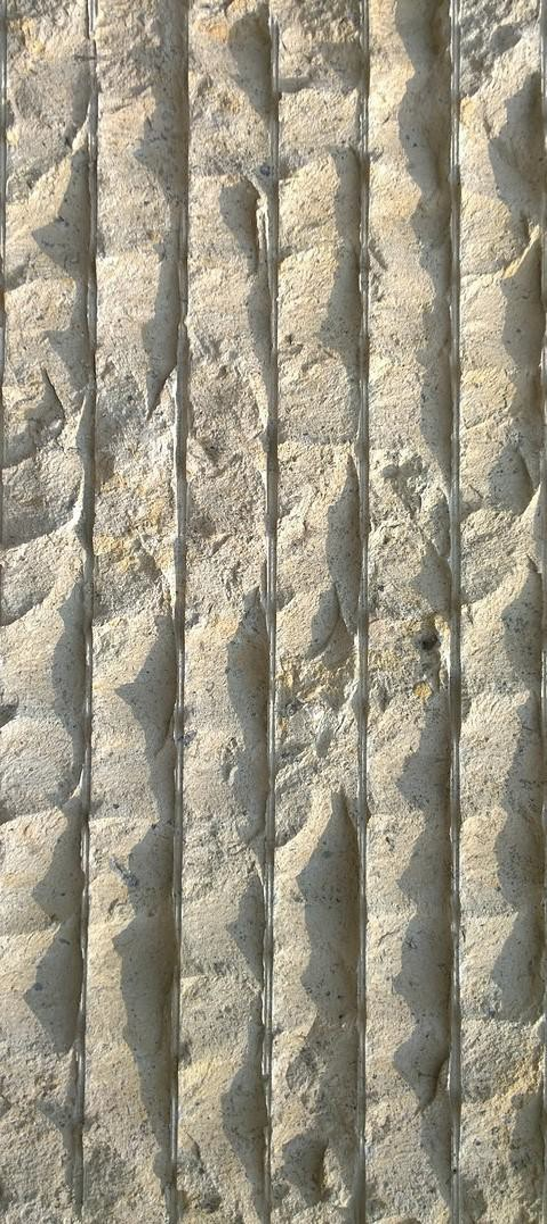 Close-up view of a stone wall with vertical metal bars embedded in the wall, intersecting the stone surface at regular intervals.
