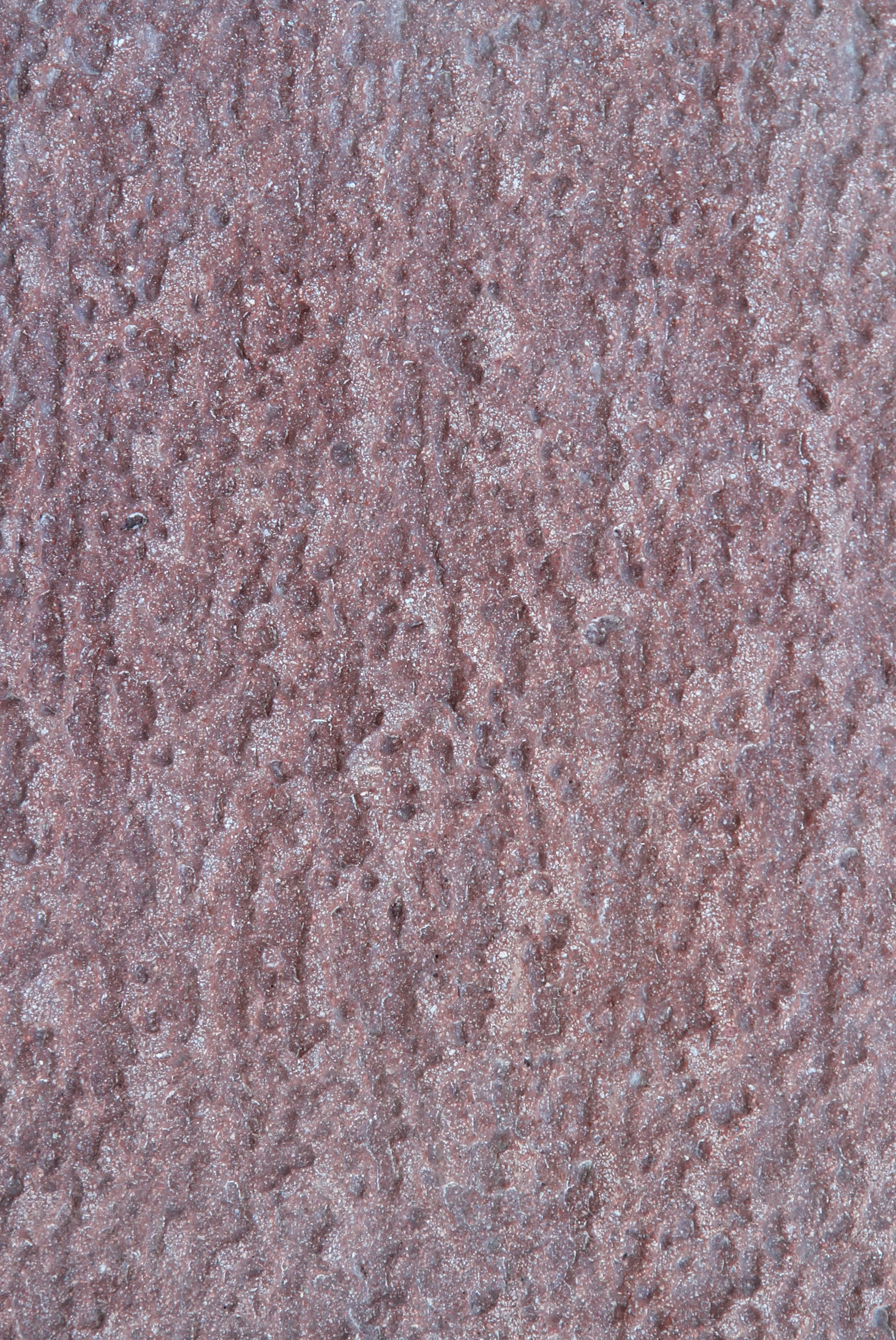 Close-up of a textured rough reddish-brown surface, possibly concrete or stone.