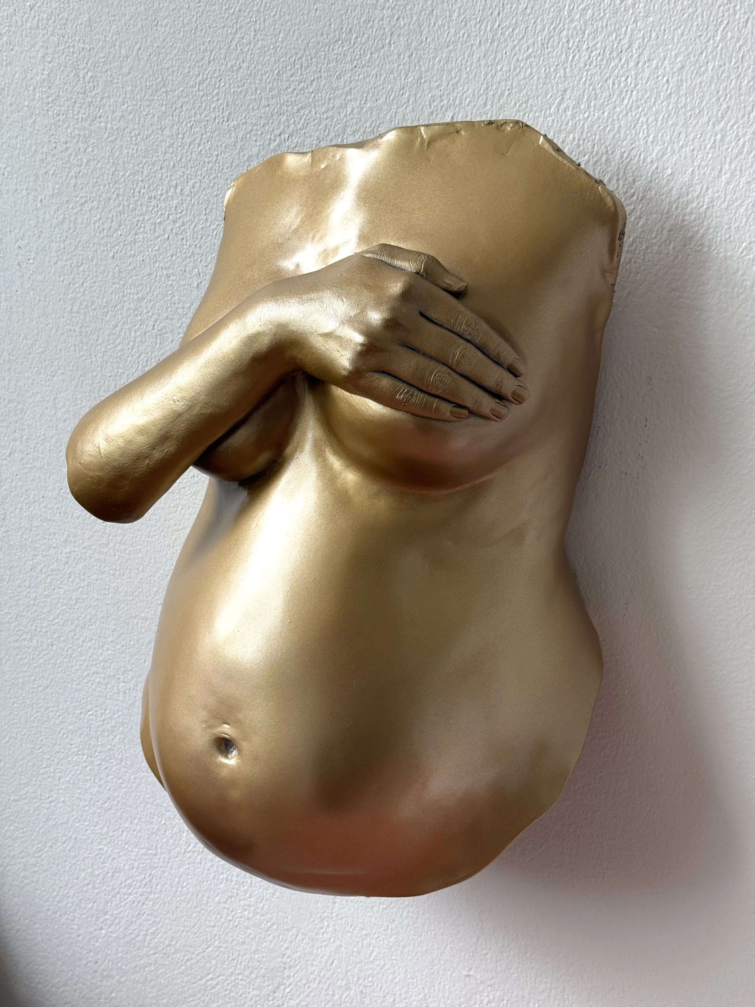 A metallic gold sculpture of a human torso with a hand covering the mouth, mounted on a wall.