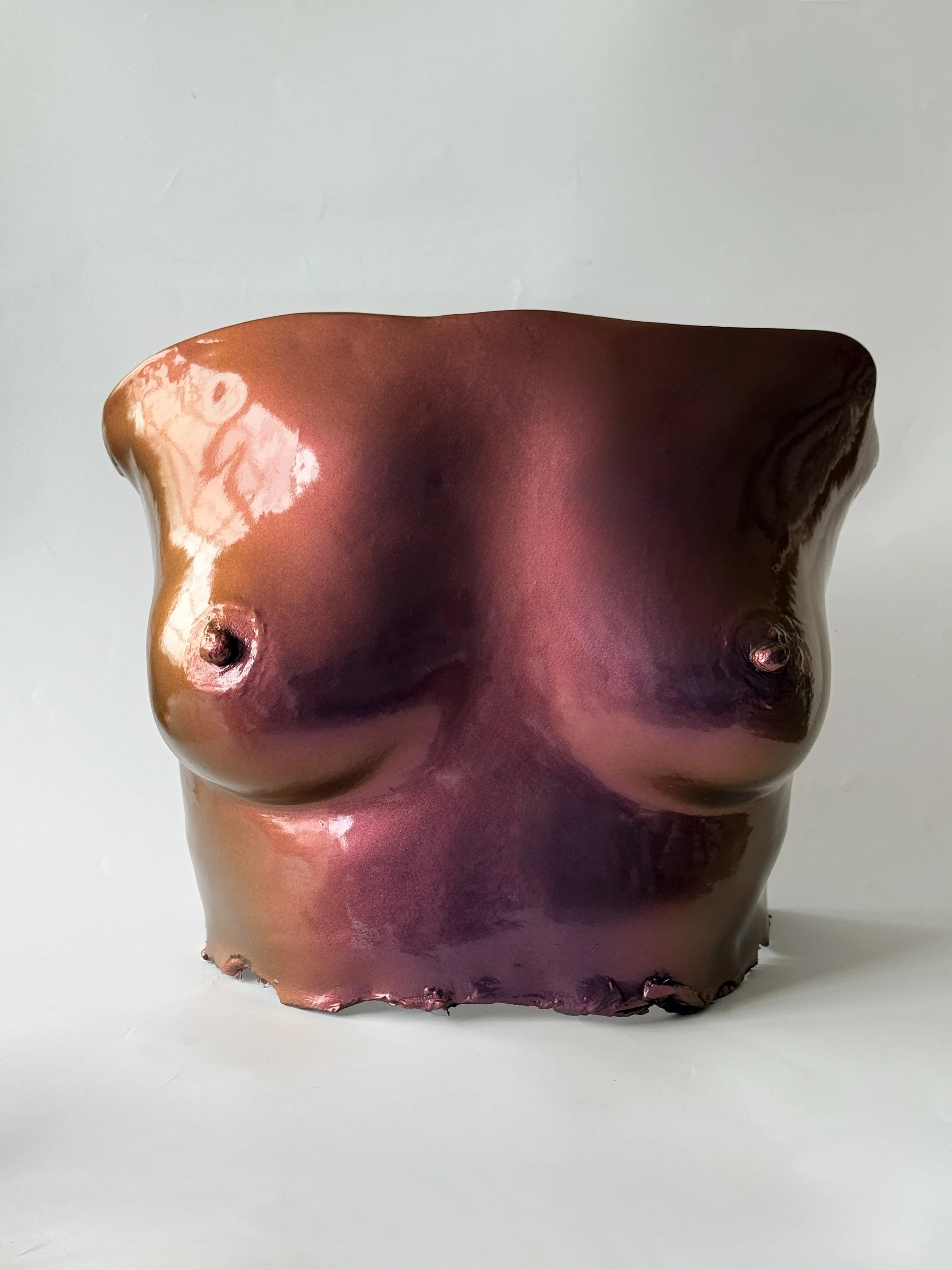 Bronze-colored ceramic sculpture of a human torso, focusing on the chest, with a smooth glossy finish and no arms or head, against a plain background.