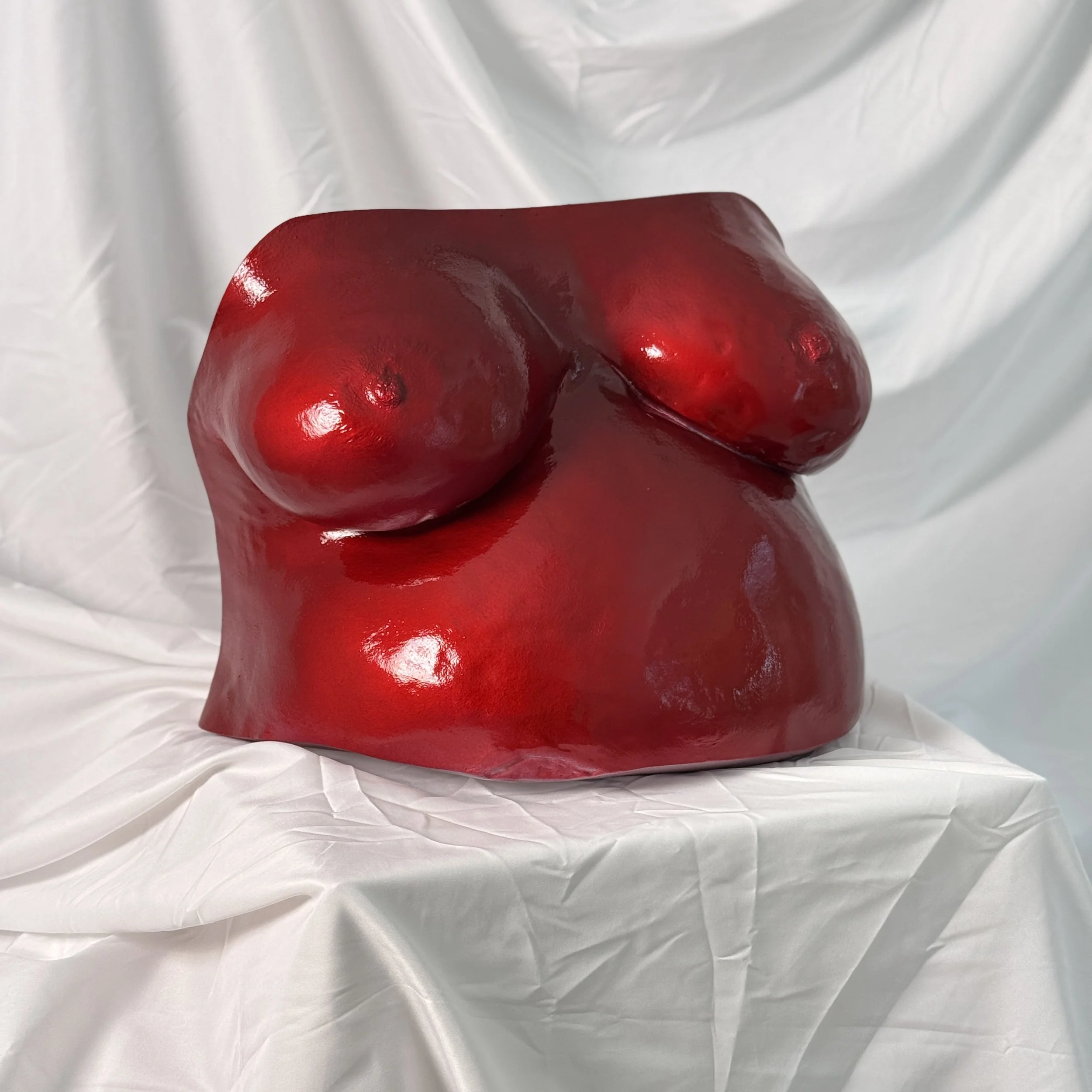 Close-up of a shiny red object with a smooth surface, resting on a white, crinkled fabric background.