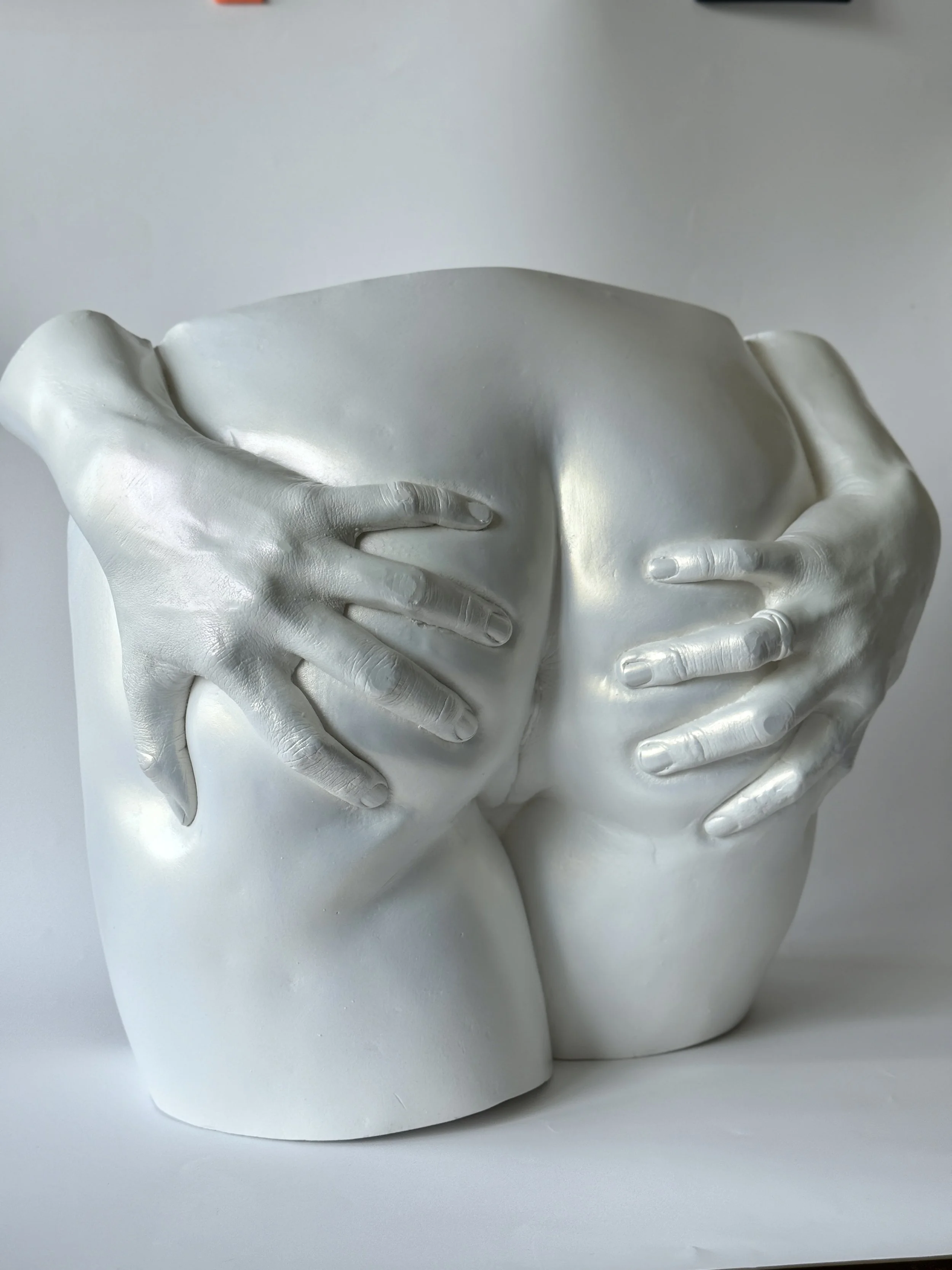 A white ceramic sculpture of a human face with closed eyes, with hands covering the face from the sides.