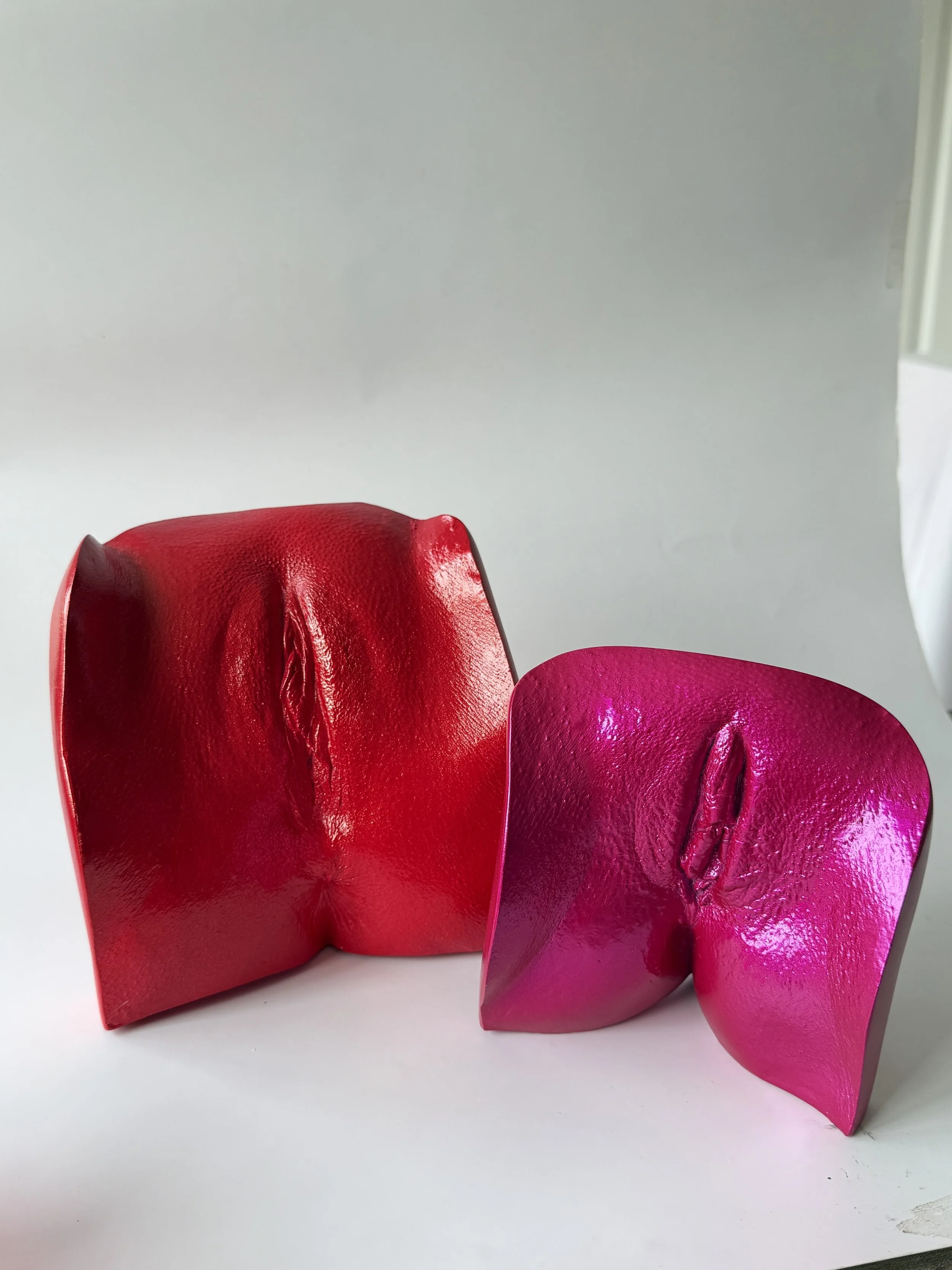 Two colorful chairs, one red and one pink, with textured leather surfaces, placed against a plain light-colored background.