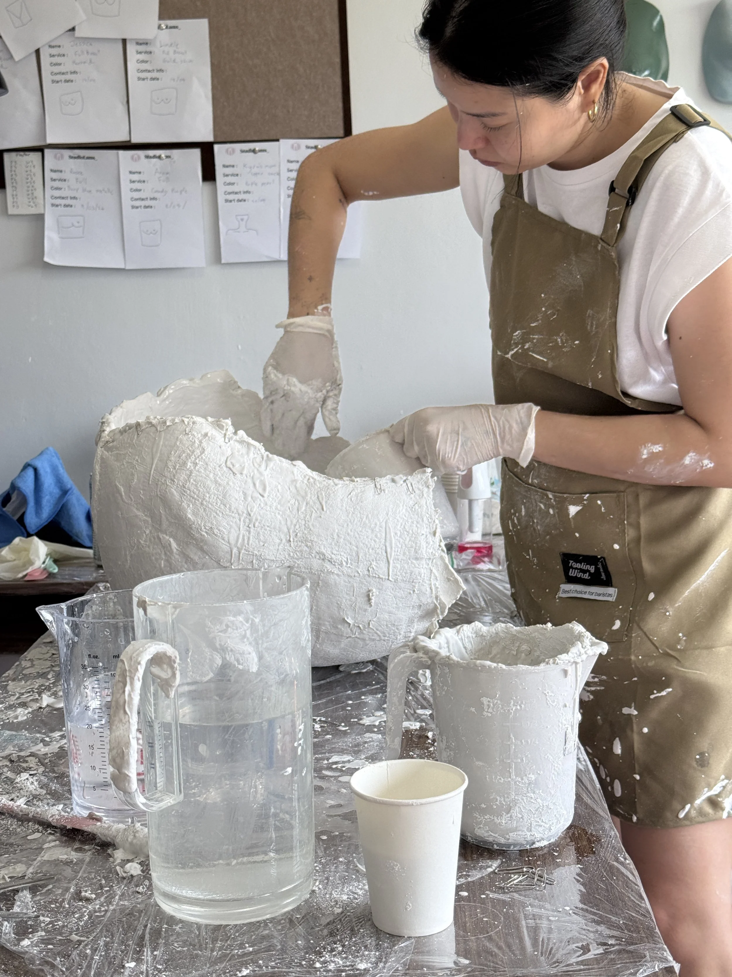 A female artist focusing on shaping and refining a large raw plaster body mold with her hands inside Studio Lams, a professional fine art lifecasting and body casting studio in Bangkok.