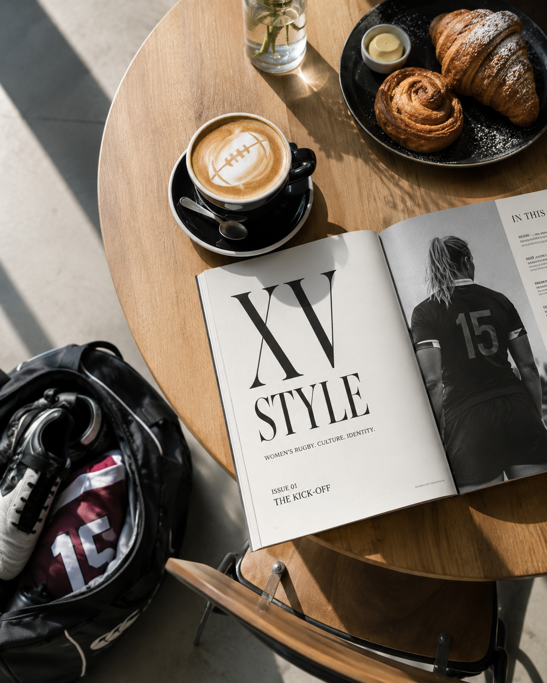 A wooden table with a black coffee in a black cup and saucer, a magazine opened to a page about women's rugby, a plate with two croissants and a small container of butter, a glass of water with a plant, and a black and white backpack nearby.