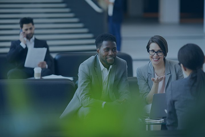 Group of four professionals in a business meeting, two men and two women, sitting at a table in an office building.